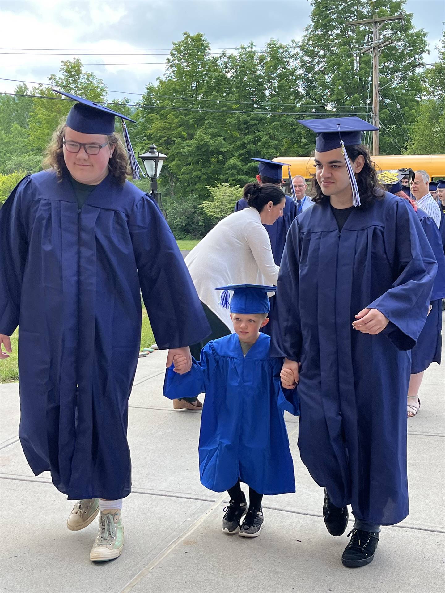 2 2023 senior graduates with a pre k student in middle dressed in caps and gowns