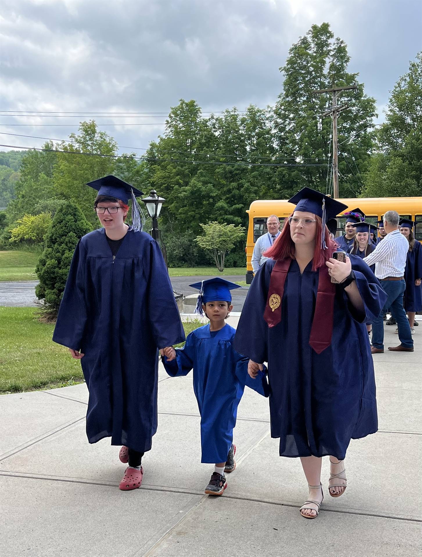 2 2023 senior graduates with a pre k student in middle dressed in caps and gowns