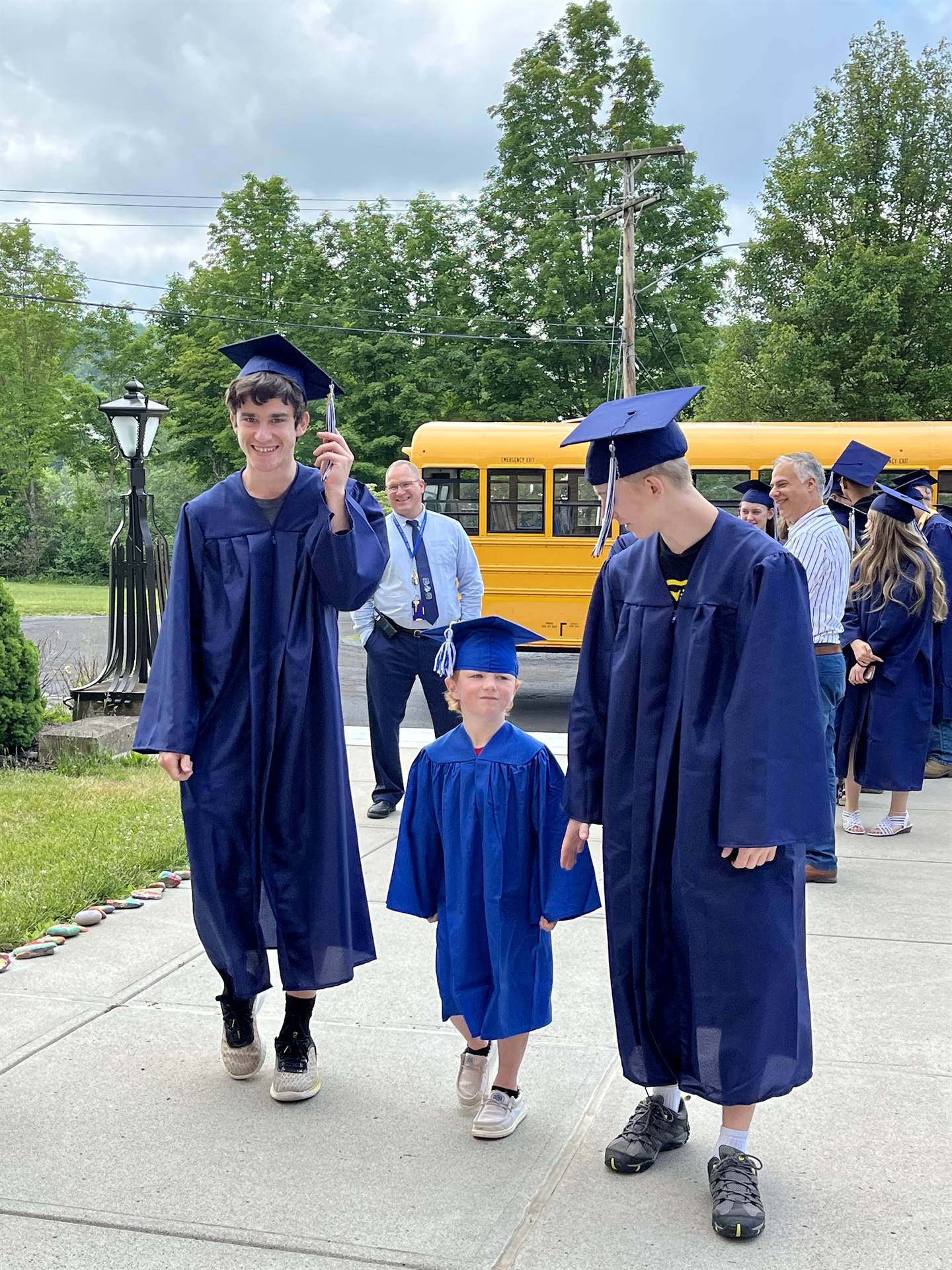 2 2023 senior graduates with a pre k student in middle dressed in caps and gowns