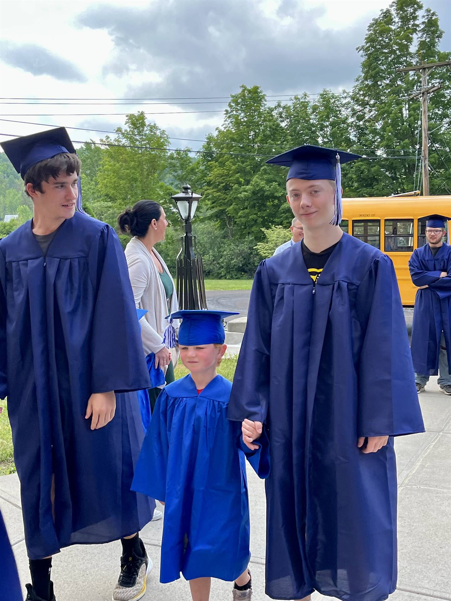 2 2023 senior graduates with a pre k student in middle dressed in caps and gowns