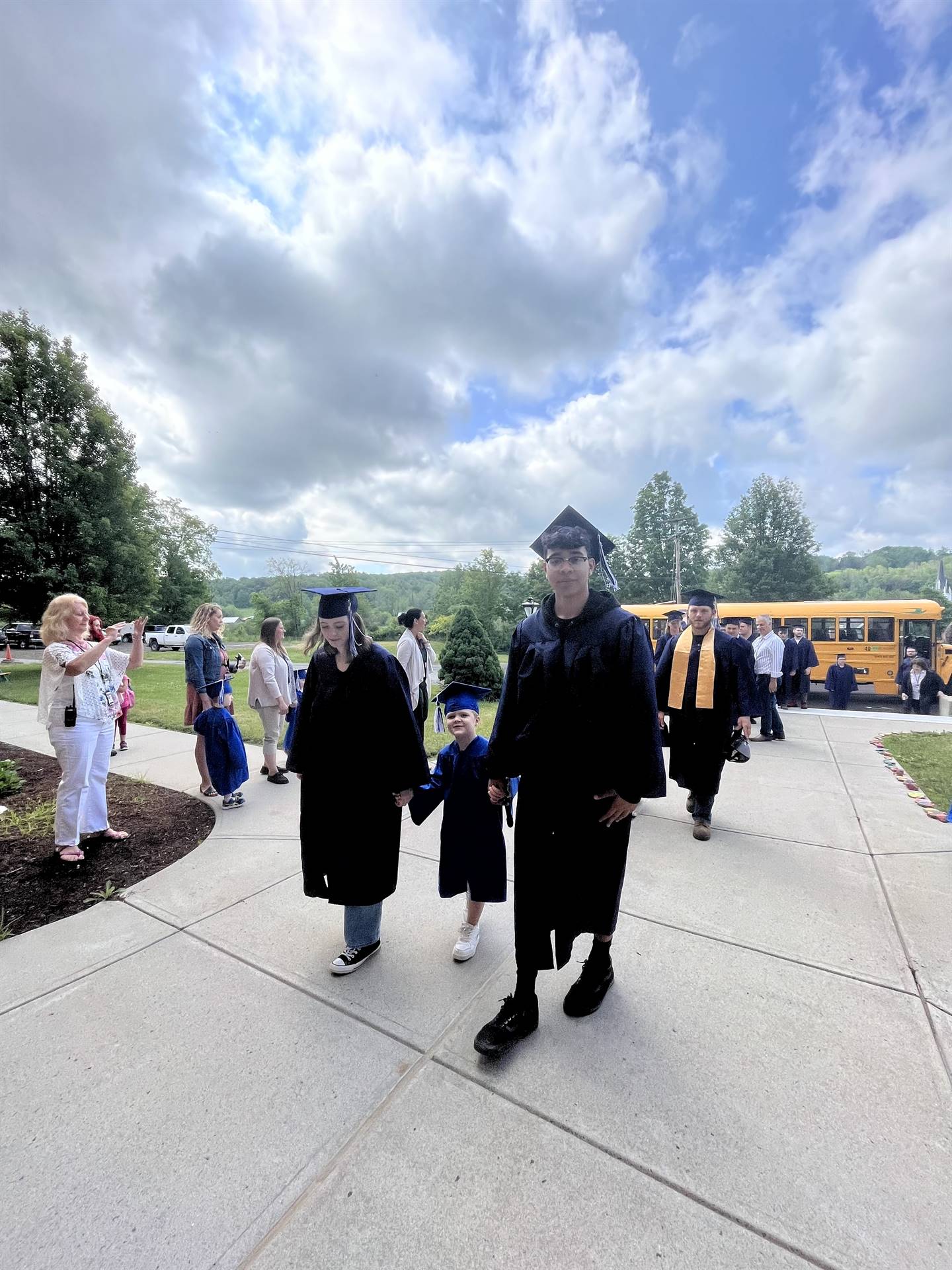 2 2023 senior graduates with a pre k student in middle dressed in caps and gowns