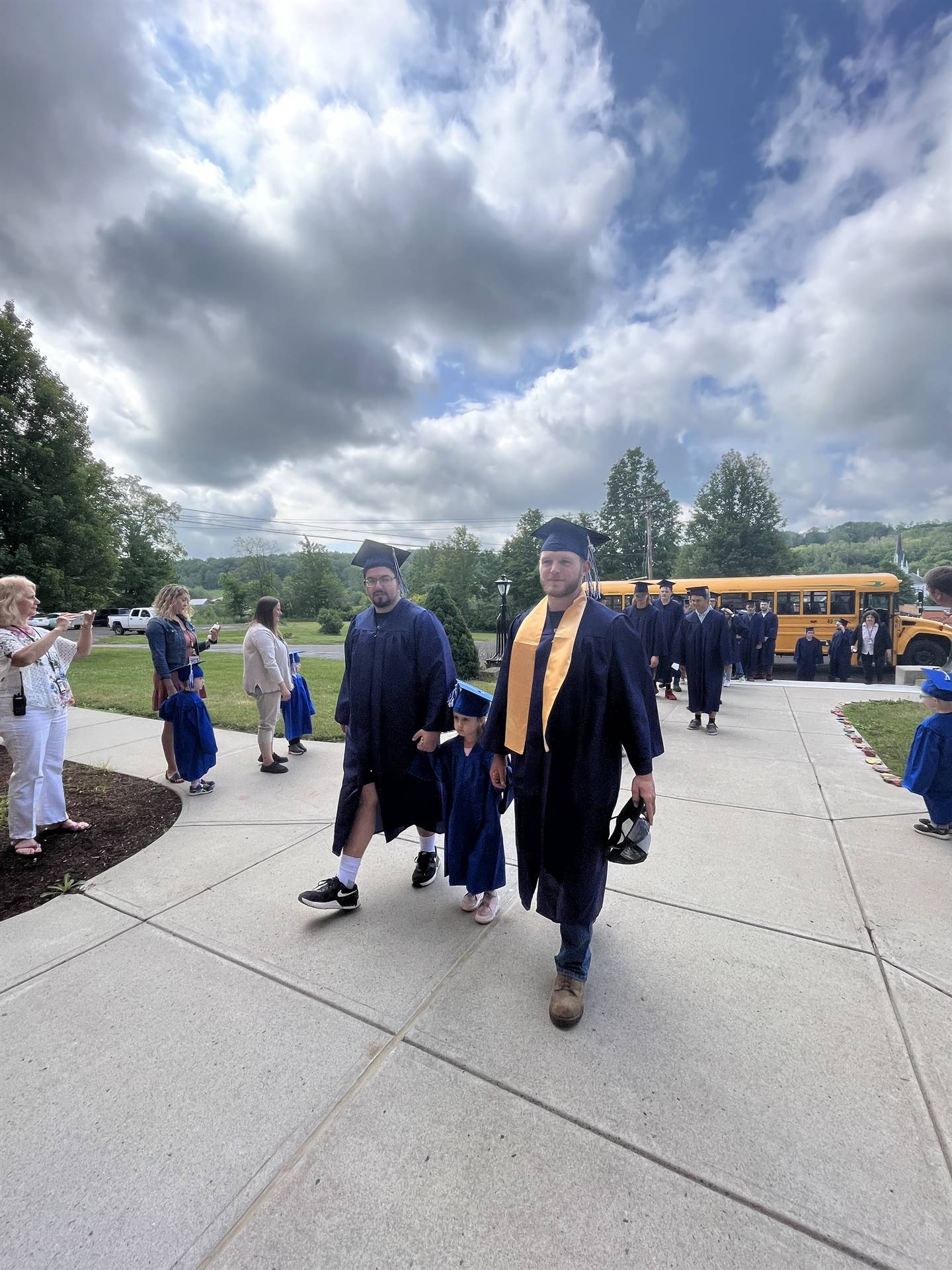 2 2023 senior graduates with a pre k student in middle dressed in caps and gowns