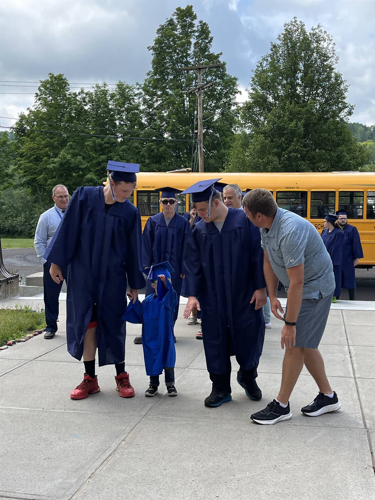 2 2023 senior graduates with a pre k student in middle dressed in caps and gowns