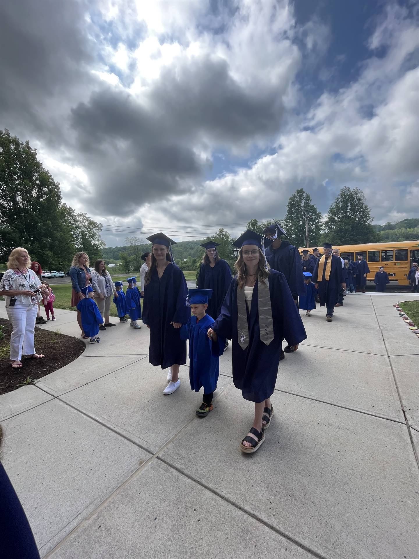 2 2023 senior graduates with a pre k student in middle dressed in caps and gowns