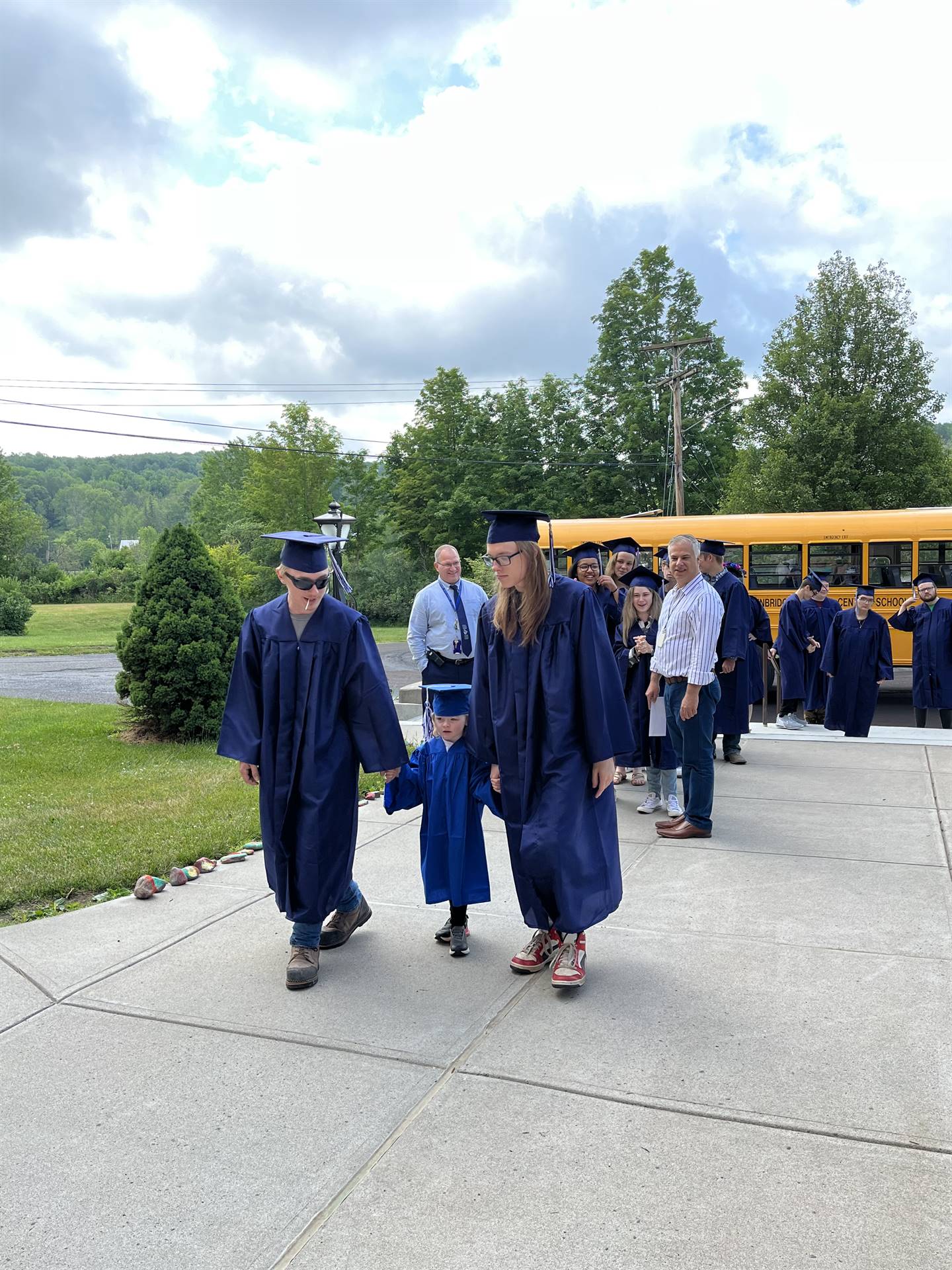 2 2023 senior graduates with a pre k student in middle dressed in caps and gowns