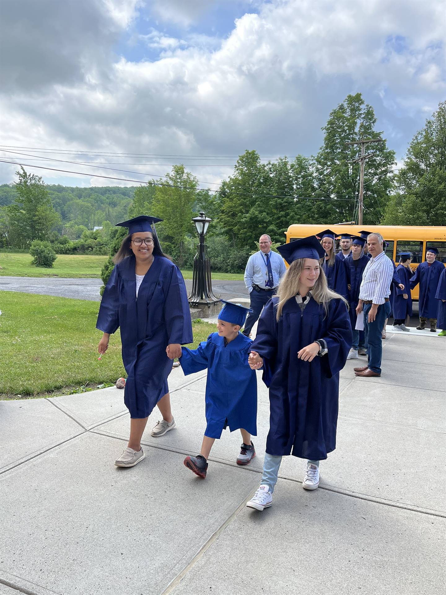 2 2023 senior graduates with a pre k student in middle dressed in caps and gowns