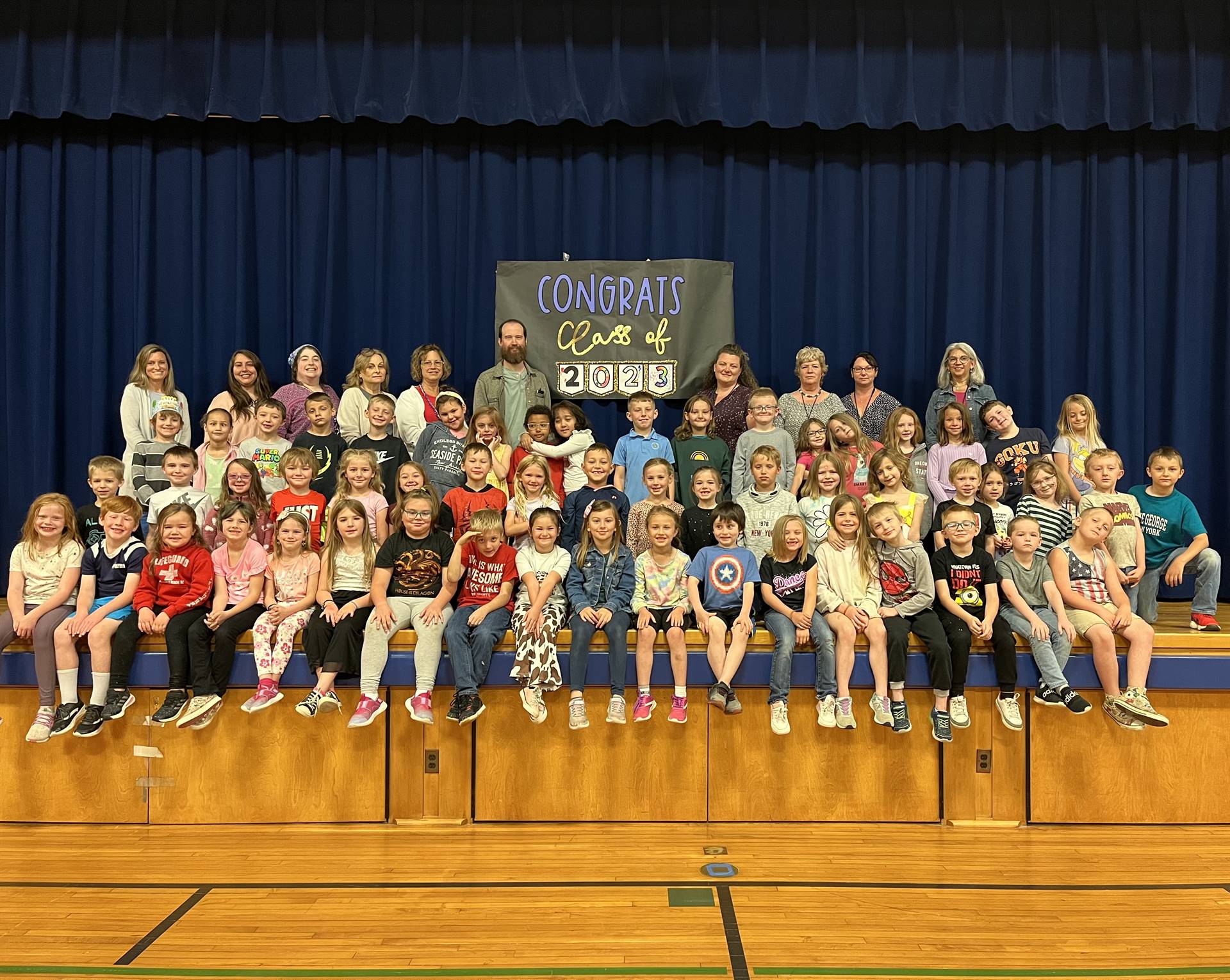 A group of children on stage with blue background and sign saying Congrats class of 2023