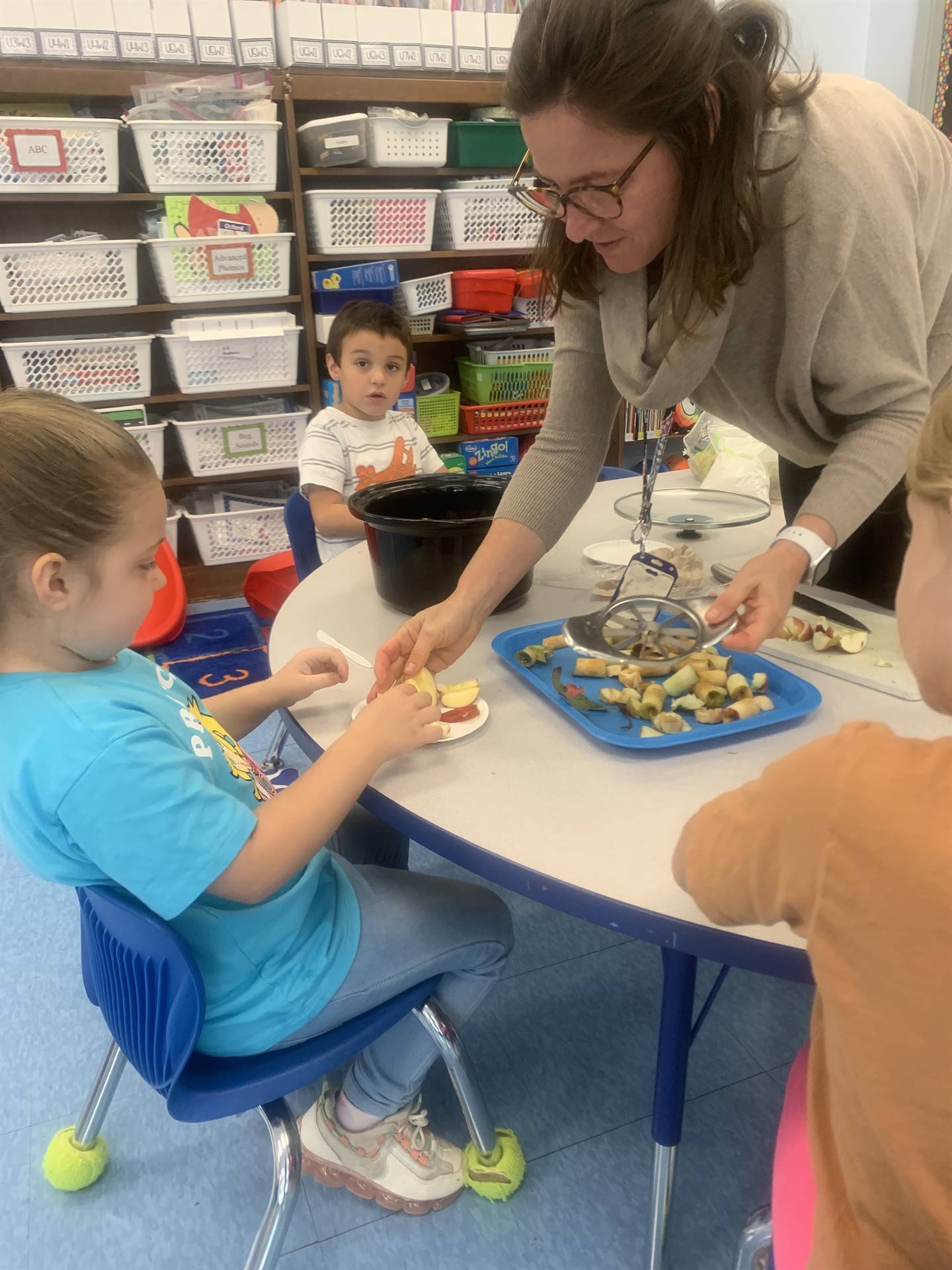 a teacher helps kids cut apples