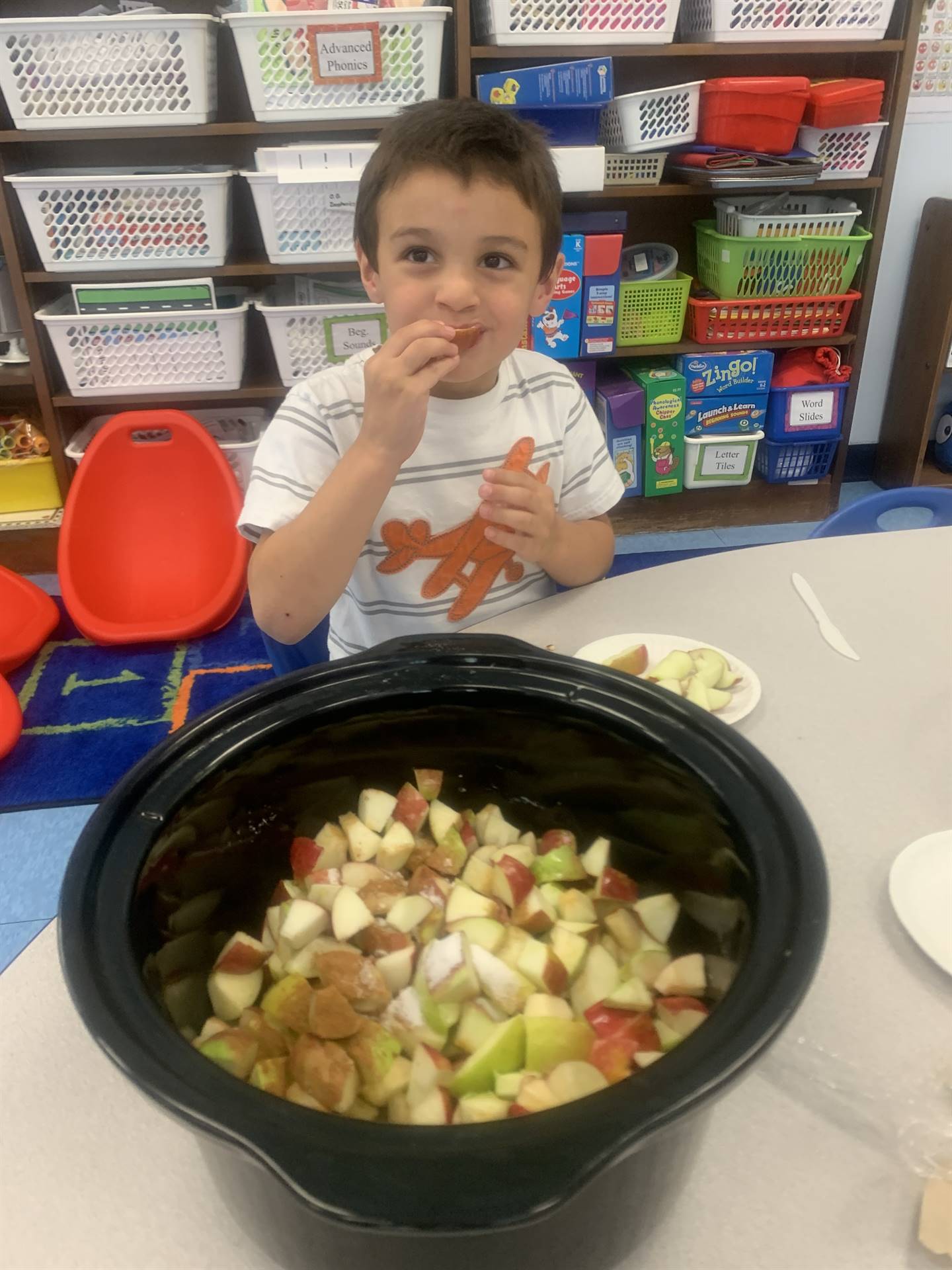 a student tastes an apple while cut apples sit in a large black pot