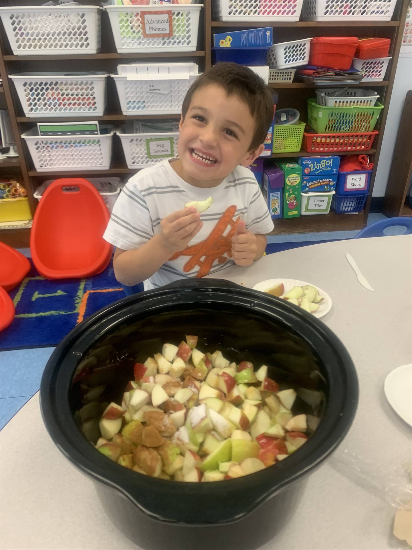 a student tastes an apple while cut apples sit in a large black pot