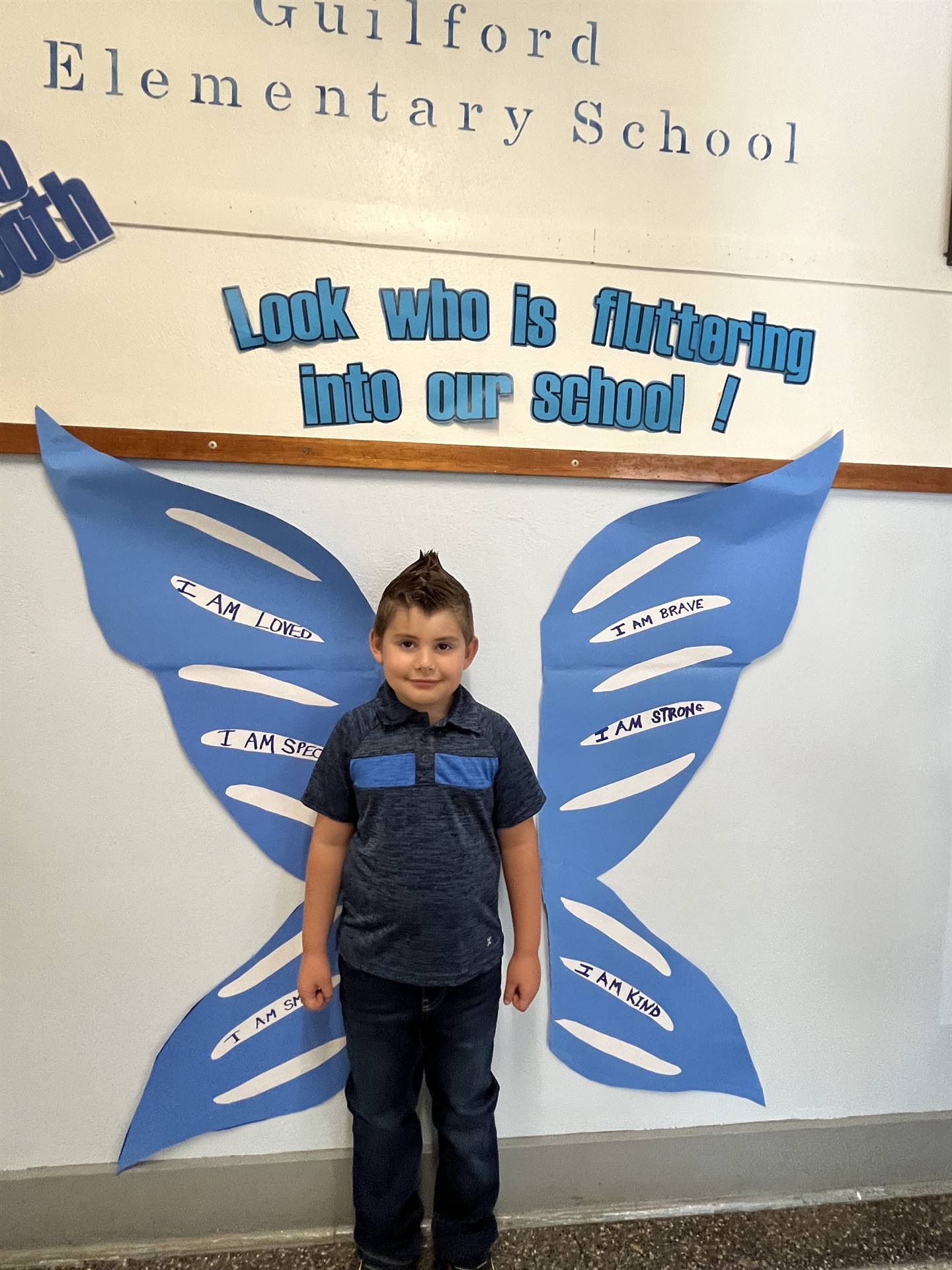 student standing between butterfly wings with sign on top saying "look who is fluttering into our sc