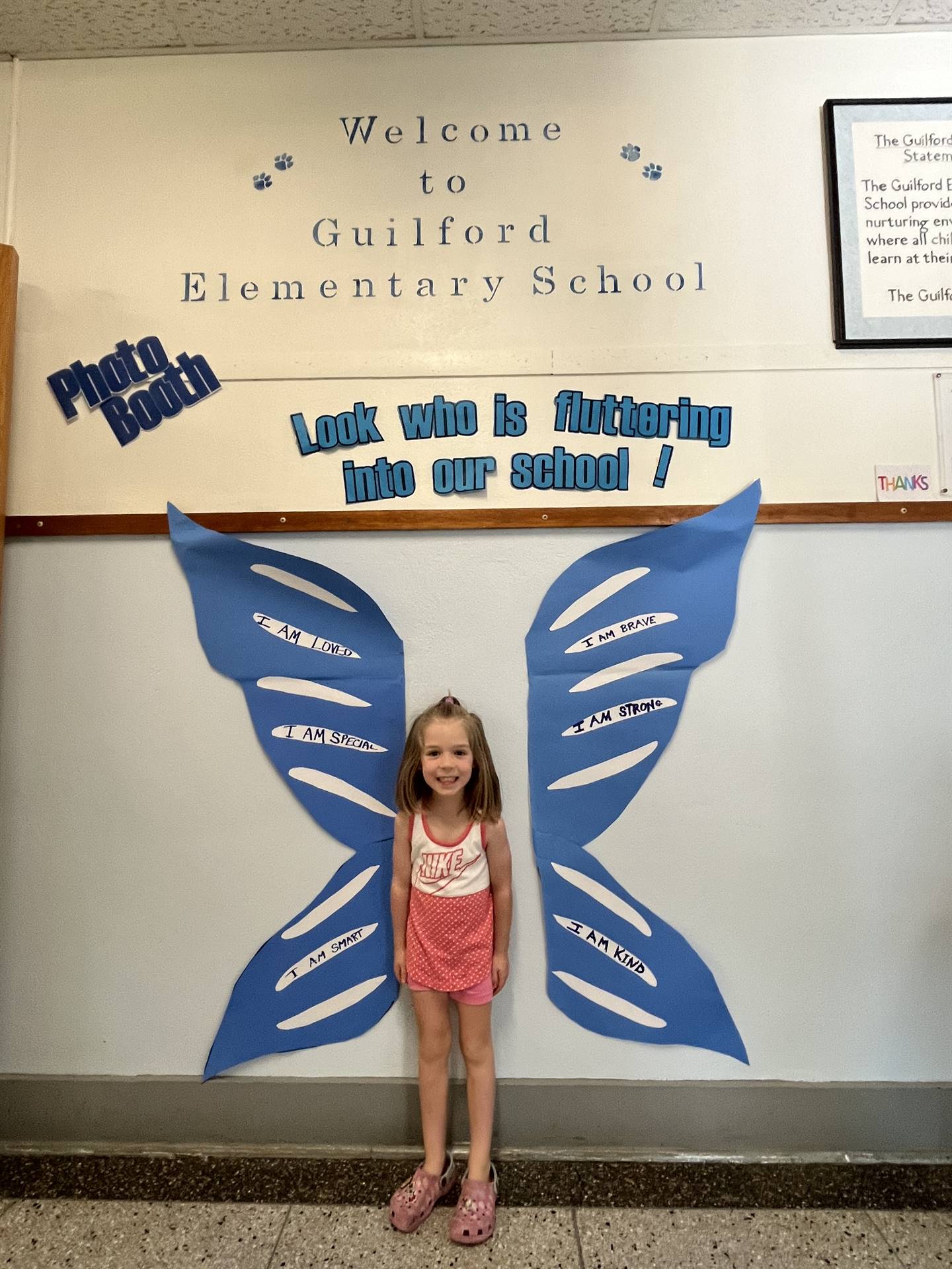 student standing between butterfly wings with sign on top saying "look who is fluttering into our sc