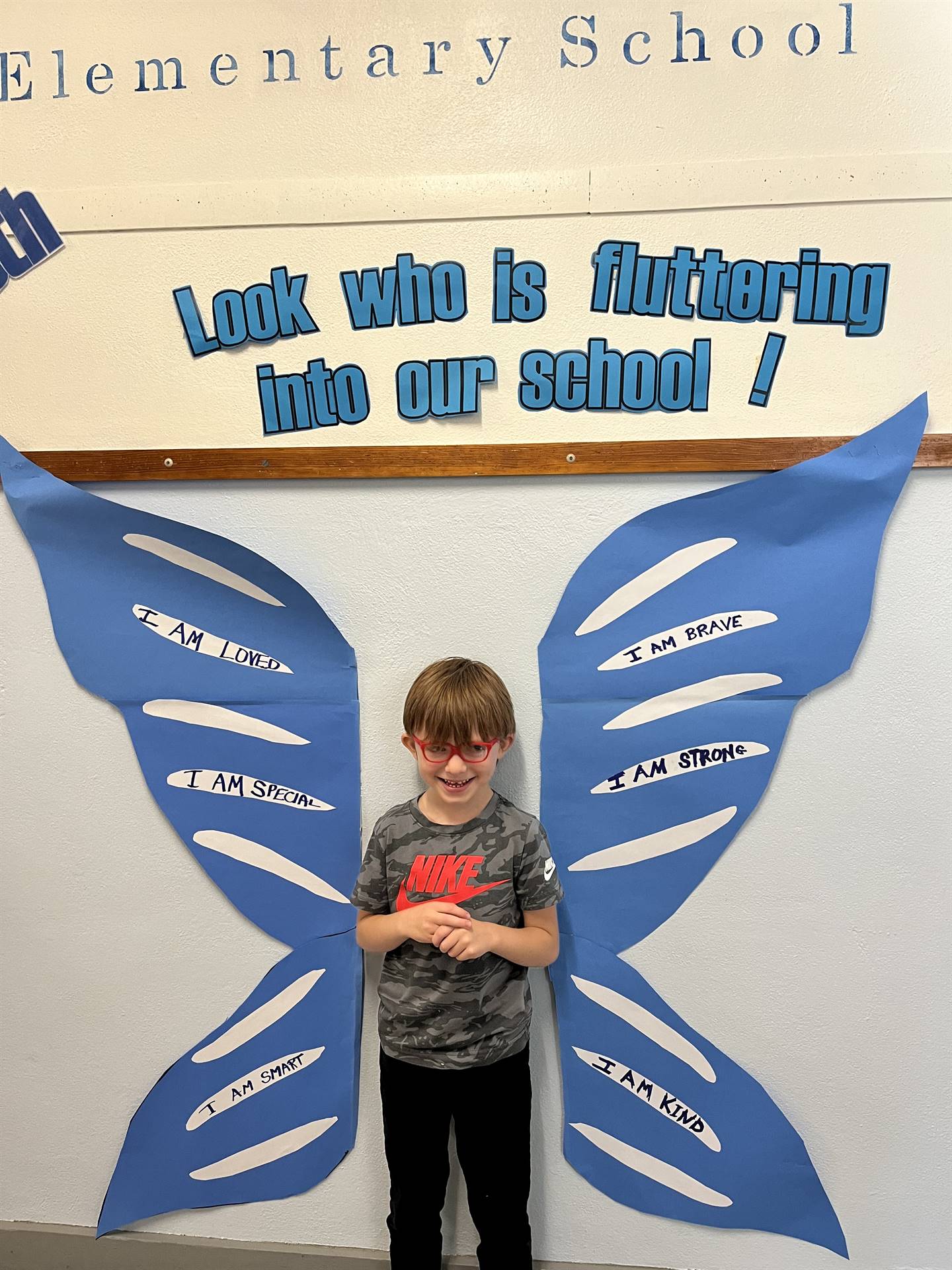 student standing between butterfly wings with sign on top saying "look who is fluttering into our sc