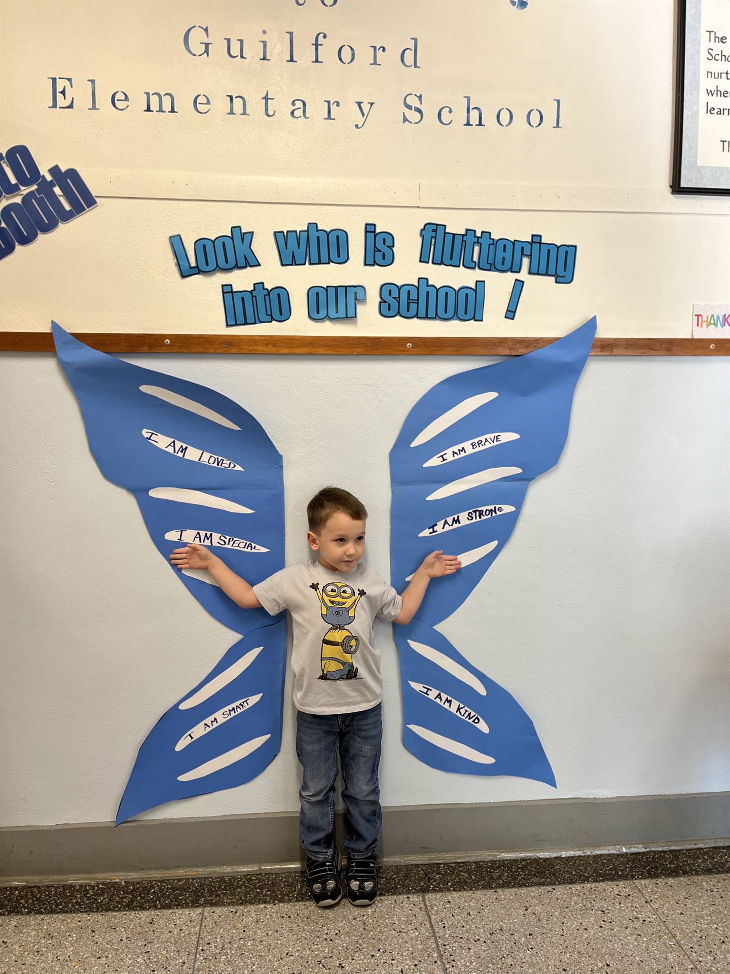 student standing between butterfly wings with sign on top saying "look who is fluttering into our sc