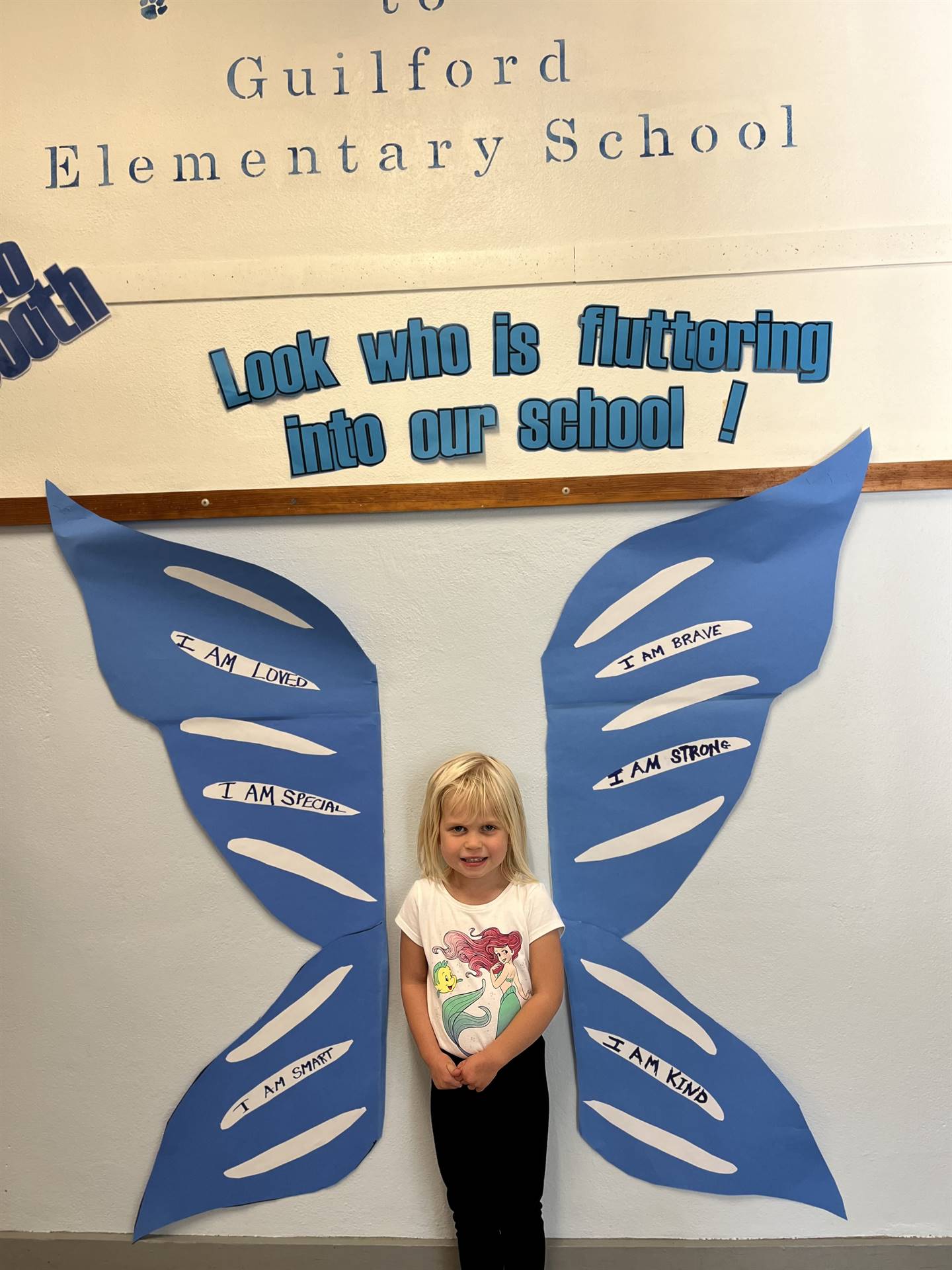 student standing between butterfly wings with sign on top saying "look who is fluttering into our sc