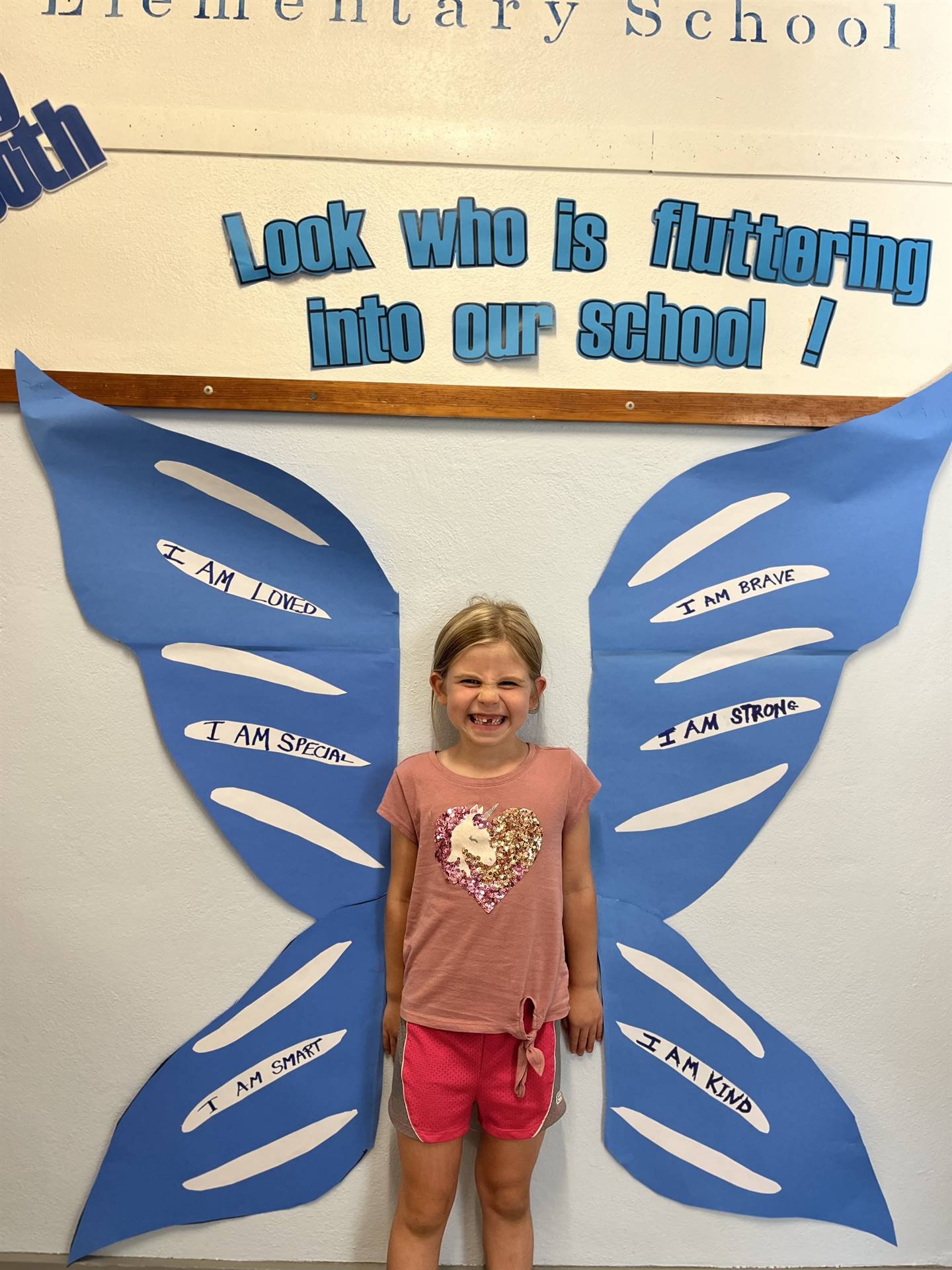 student standing between butterfly wings with sign on top saying "look who is fluttering into our sc