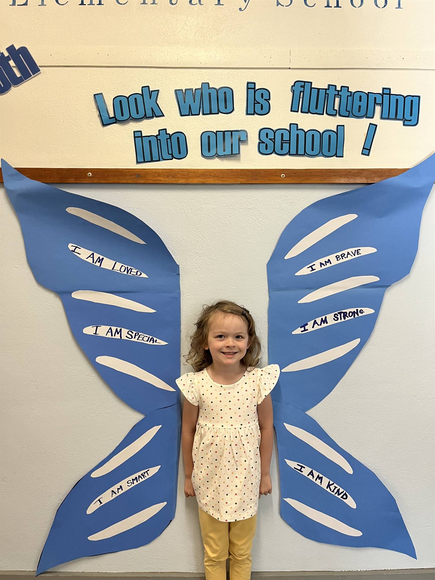 student standing between butterfly wings with sign on top saying "look who is fluttering into our sc