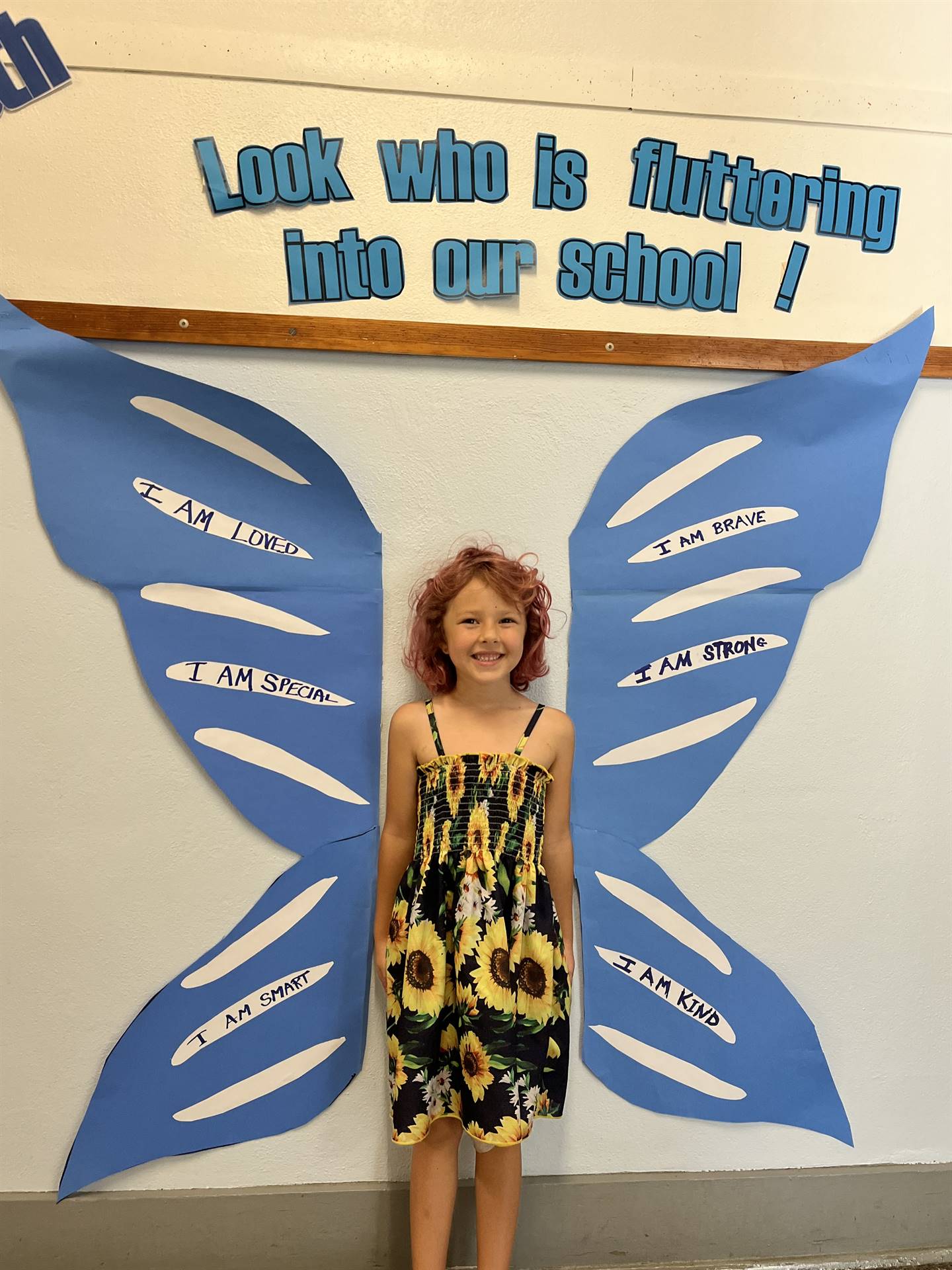 student standing between butterfly wings with sign on top saying "look who is fluttering into our sc