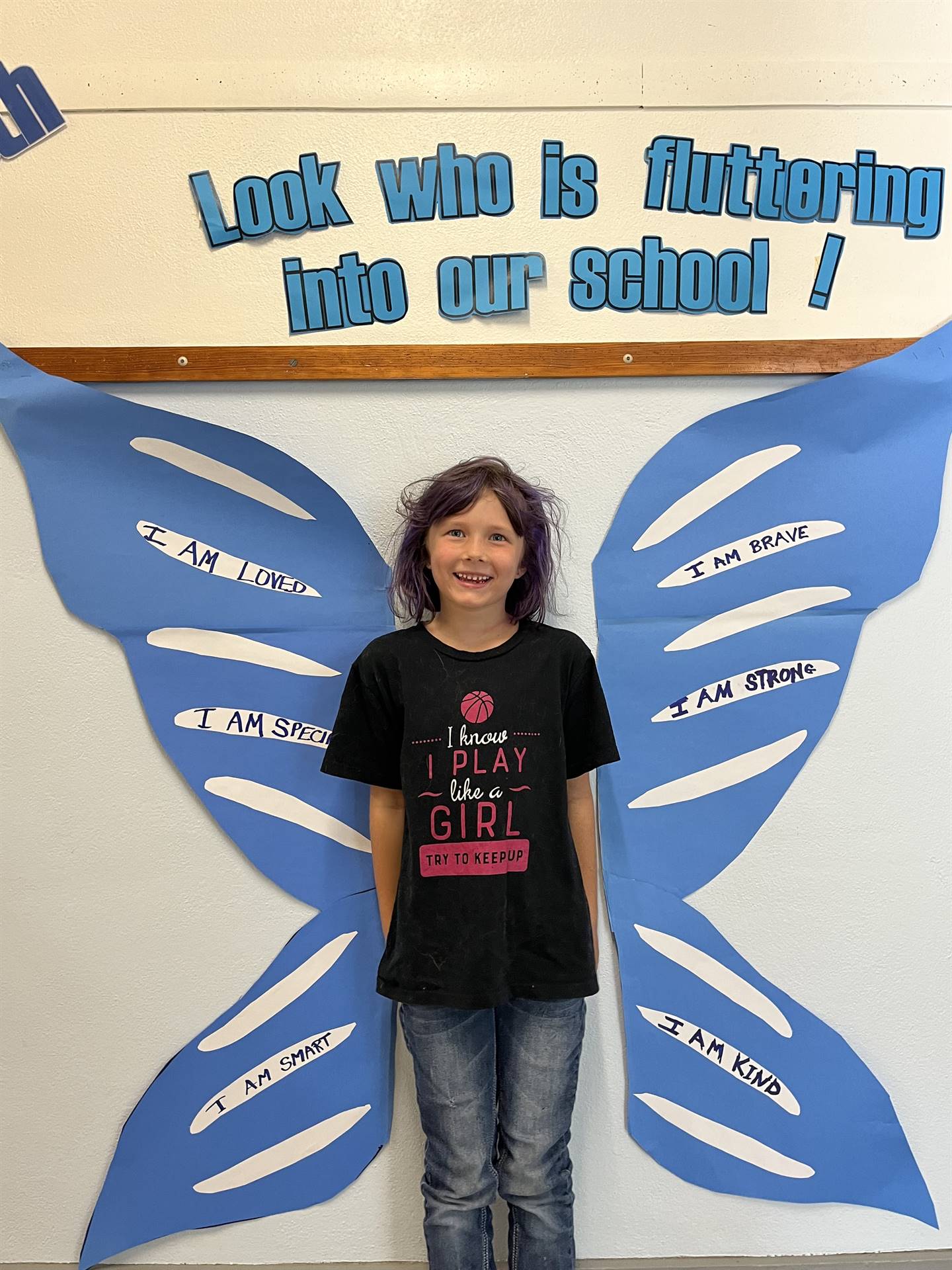 student standing between butterfly wings with sign on top saying "look who is fluttering into our sc