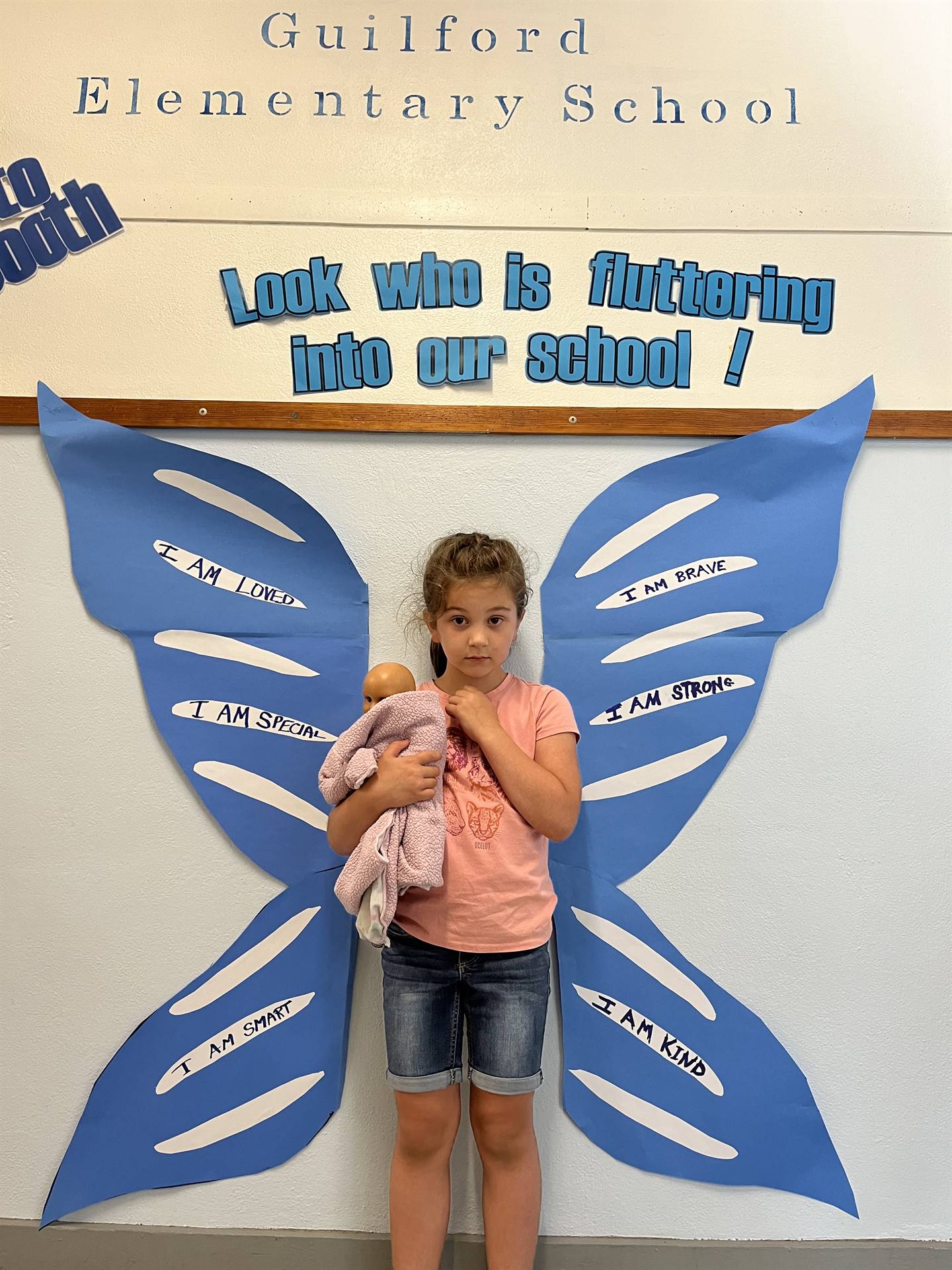 student standing between butterfly wings with sign on top saying "look who is fluttering into our sc