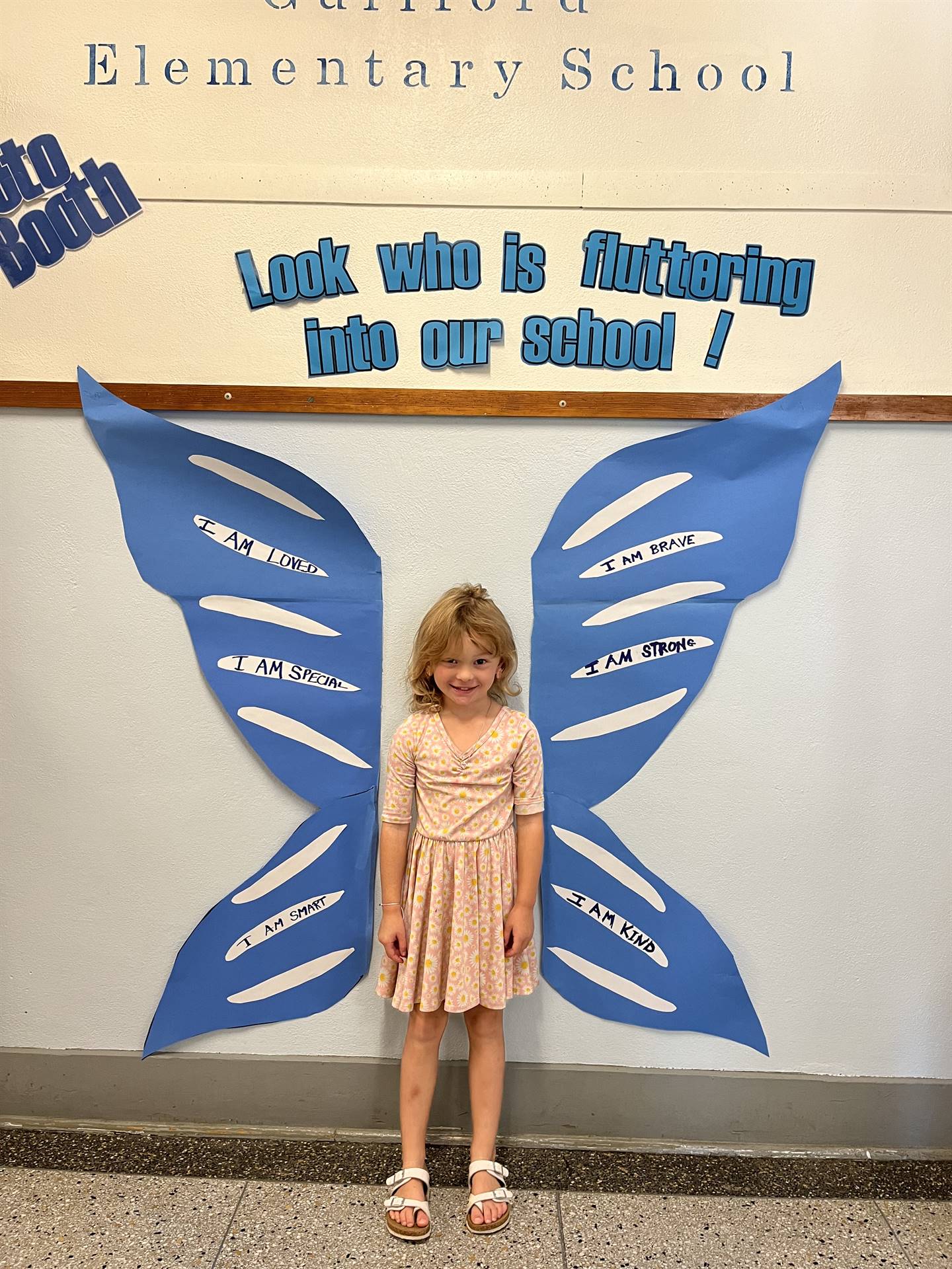 student standing between butterfly wings with sign on top saying "look who is fluttering into our sc