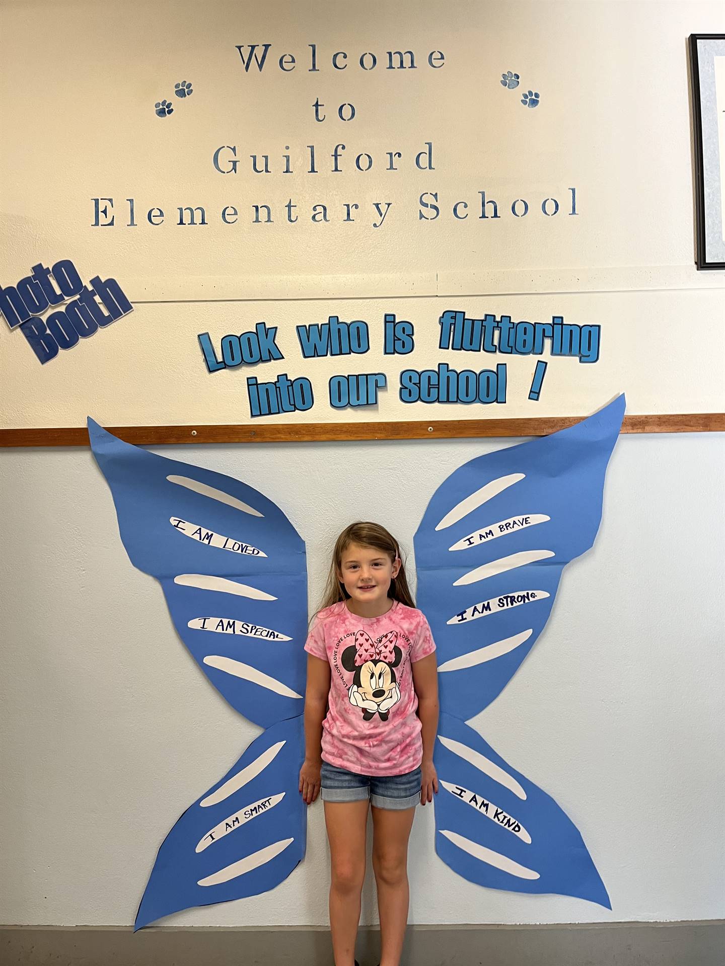 student standing between butterfly wings with sign on top saying "look who is fluttering into our sc