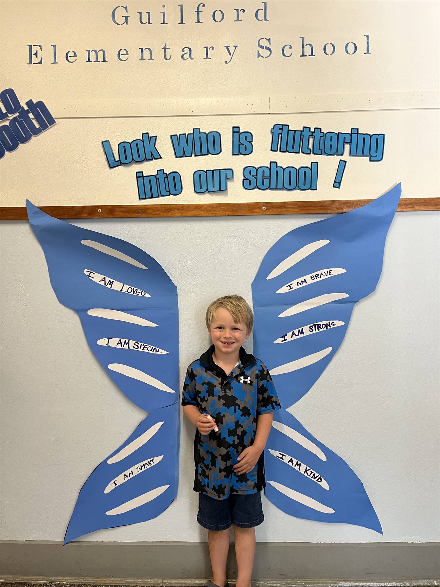 student standing between butterfly wings with sign on top saying "look who is fluttering into our sc