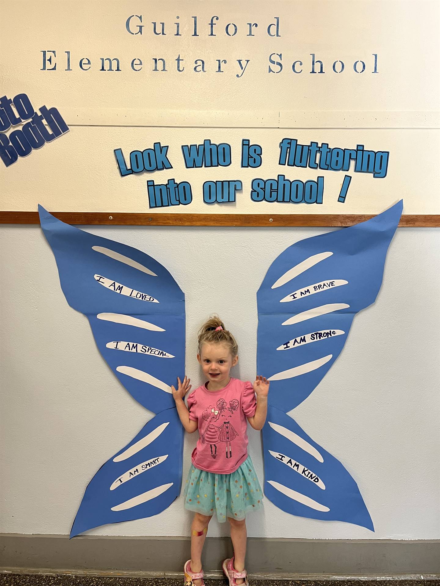 student standing between butterfly wings with sign on top saying "look who is fluttering into our sc