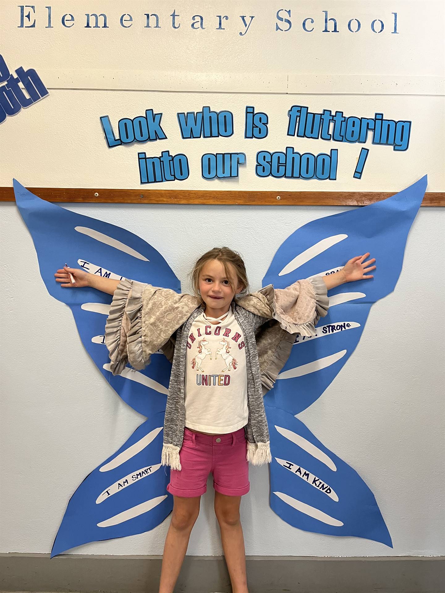 student standing between butterfly wings with sign on top saying "look who is fluttering into our sc