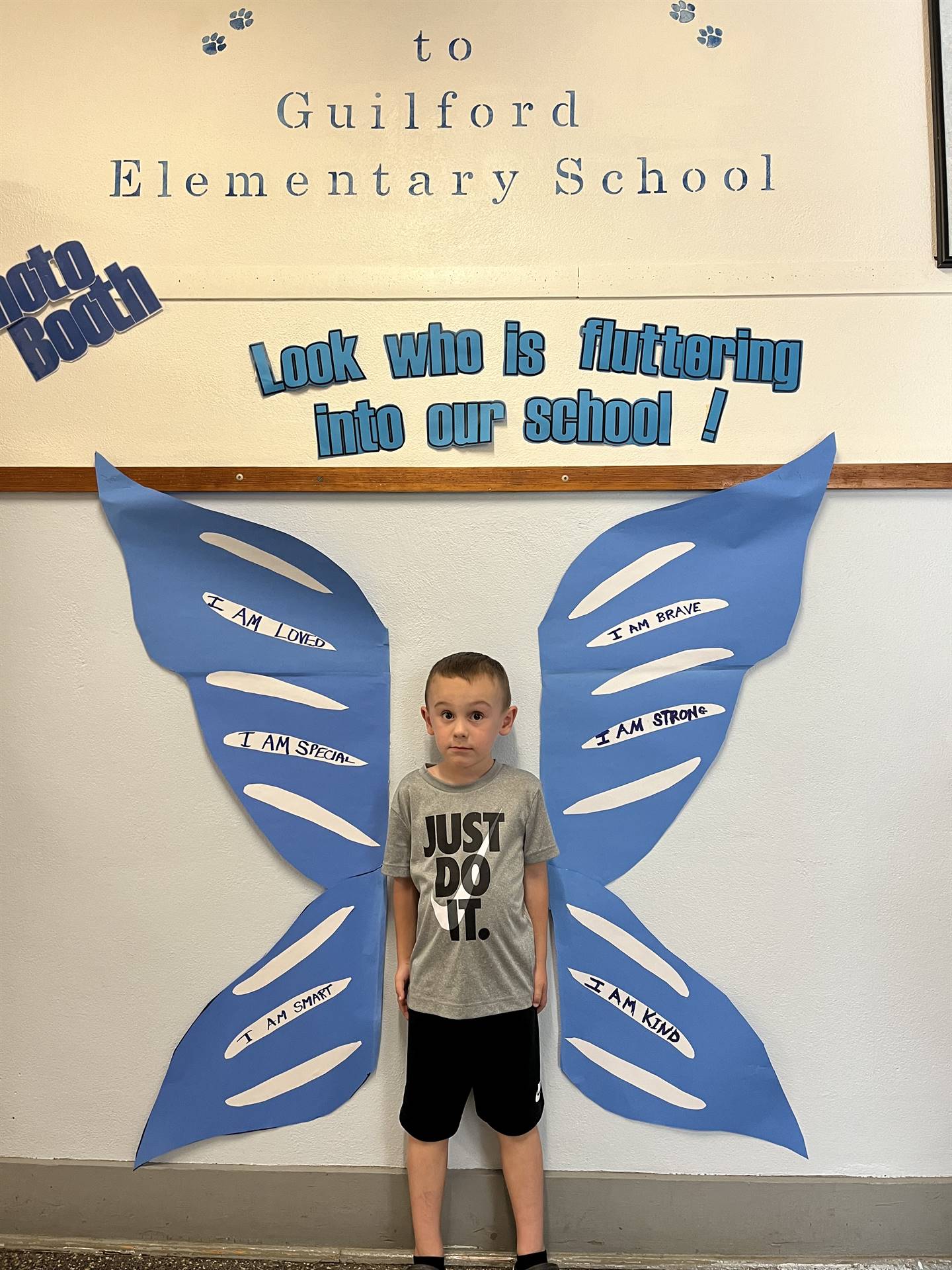 student standing between butterfly wings with sign on top saying "look who is fluttering into our sc