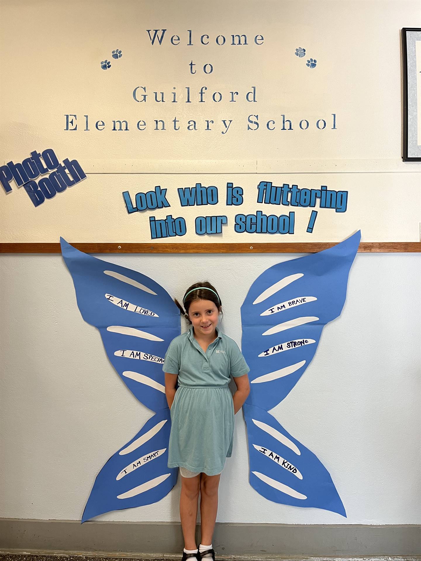 student standing between butterfly wings with sign on top saying "look who is fluttering into our sc