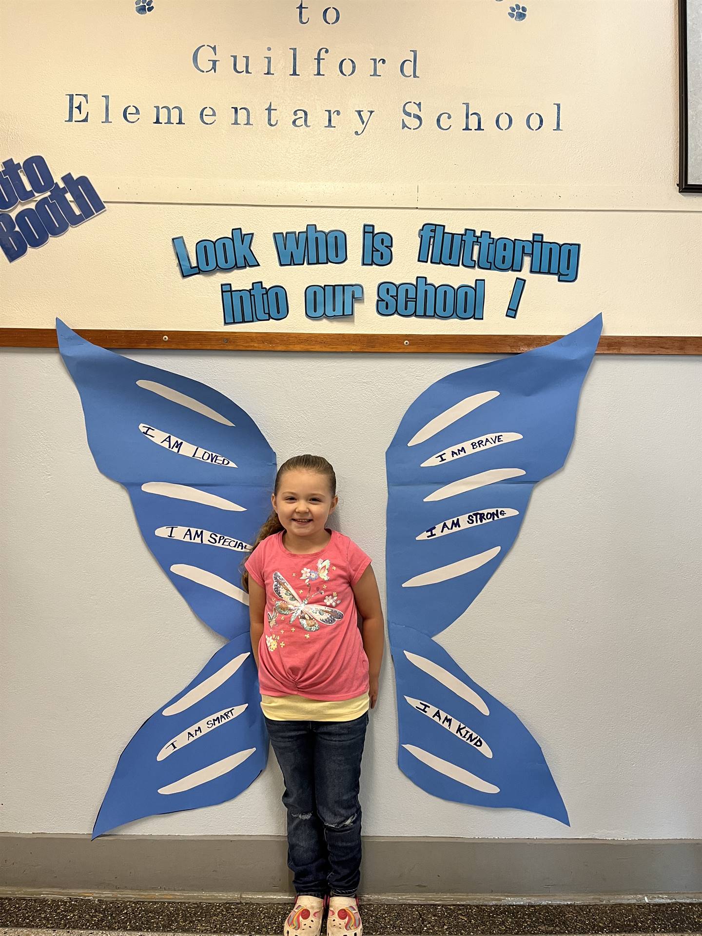 student standing between butterfly wings with sign on top saying "look who is fluttering into our sc