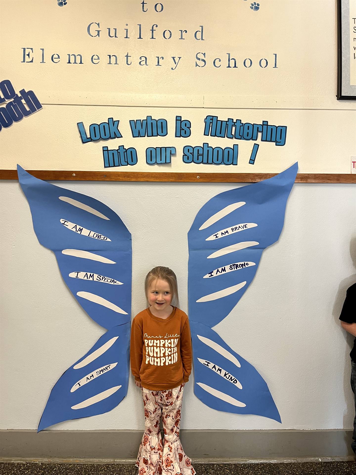 student standing between butterfly wings with sign on top saying "look who is fluttering into our sc