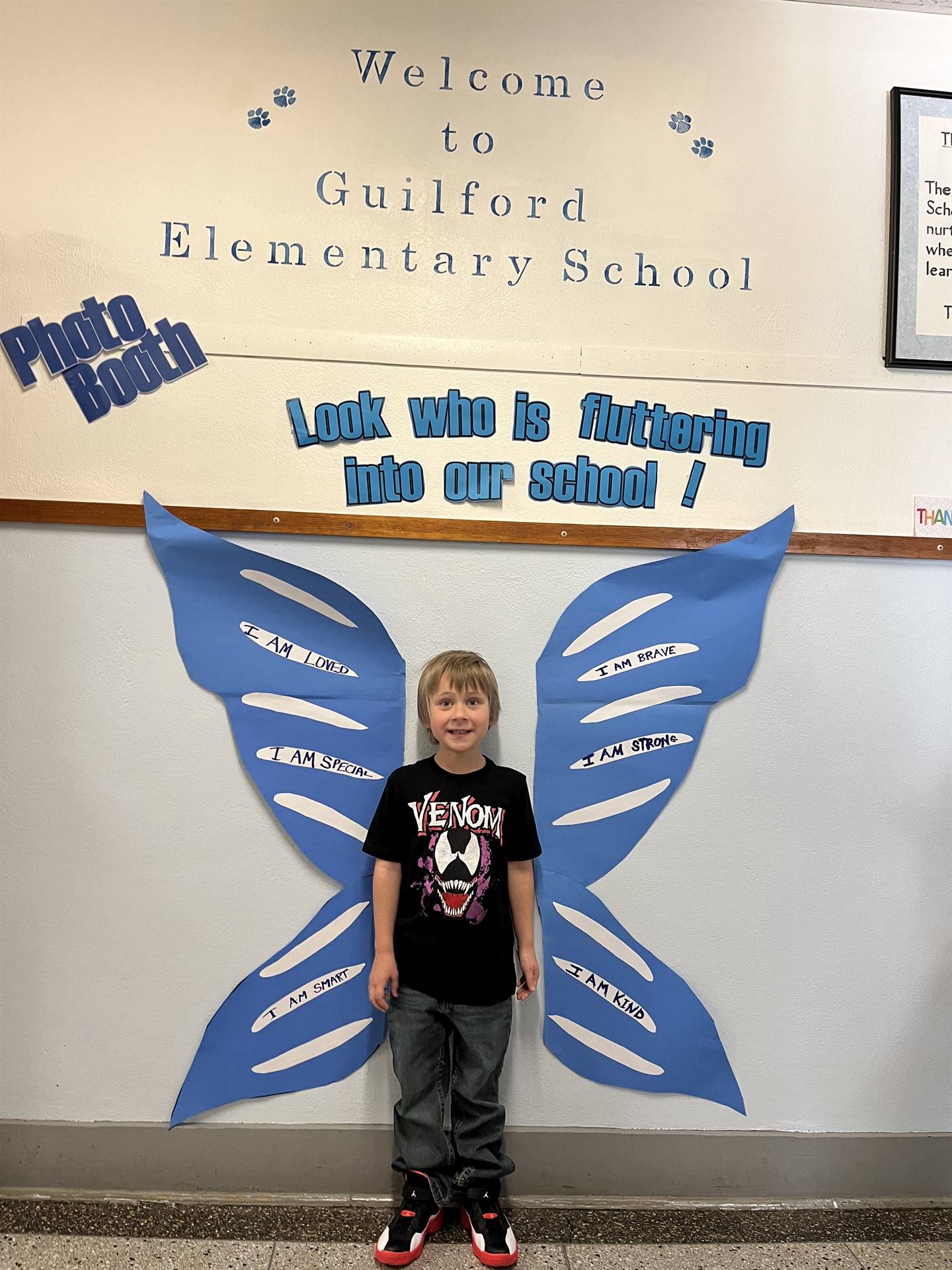 student standing between butterfly wings with sign on top saying "look who is fluttering into our sc