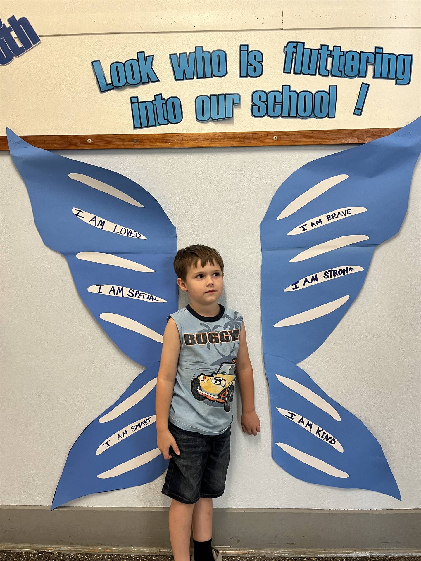 student standing between butterfly wings with sign on top saying "look who is fluttering into our sc