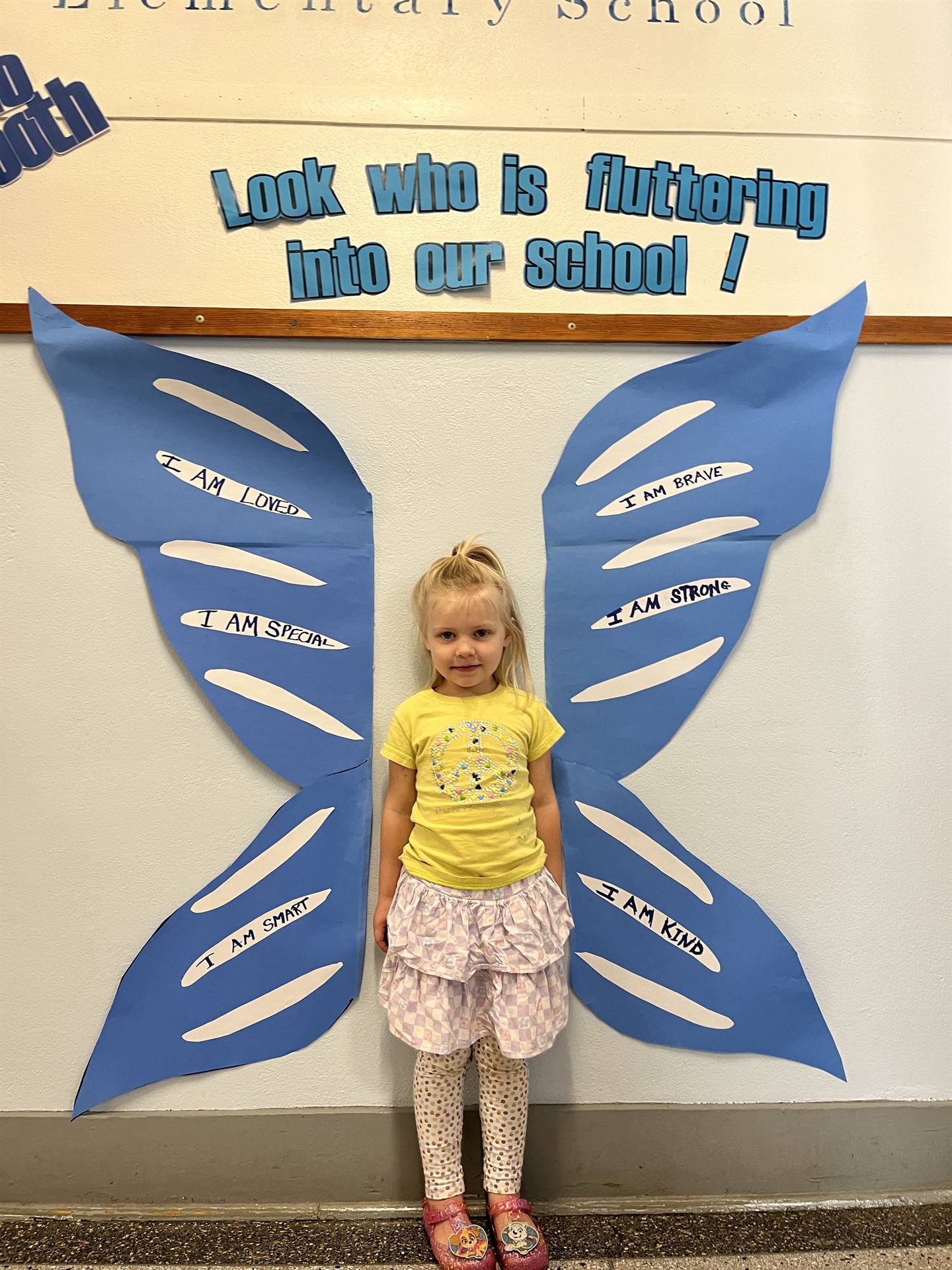 student standing between butterfly wings with sign on top saying "look who is fluttering into our sc