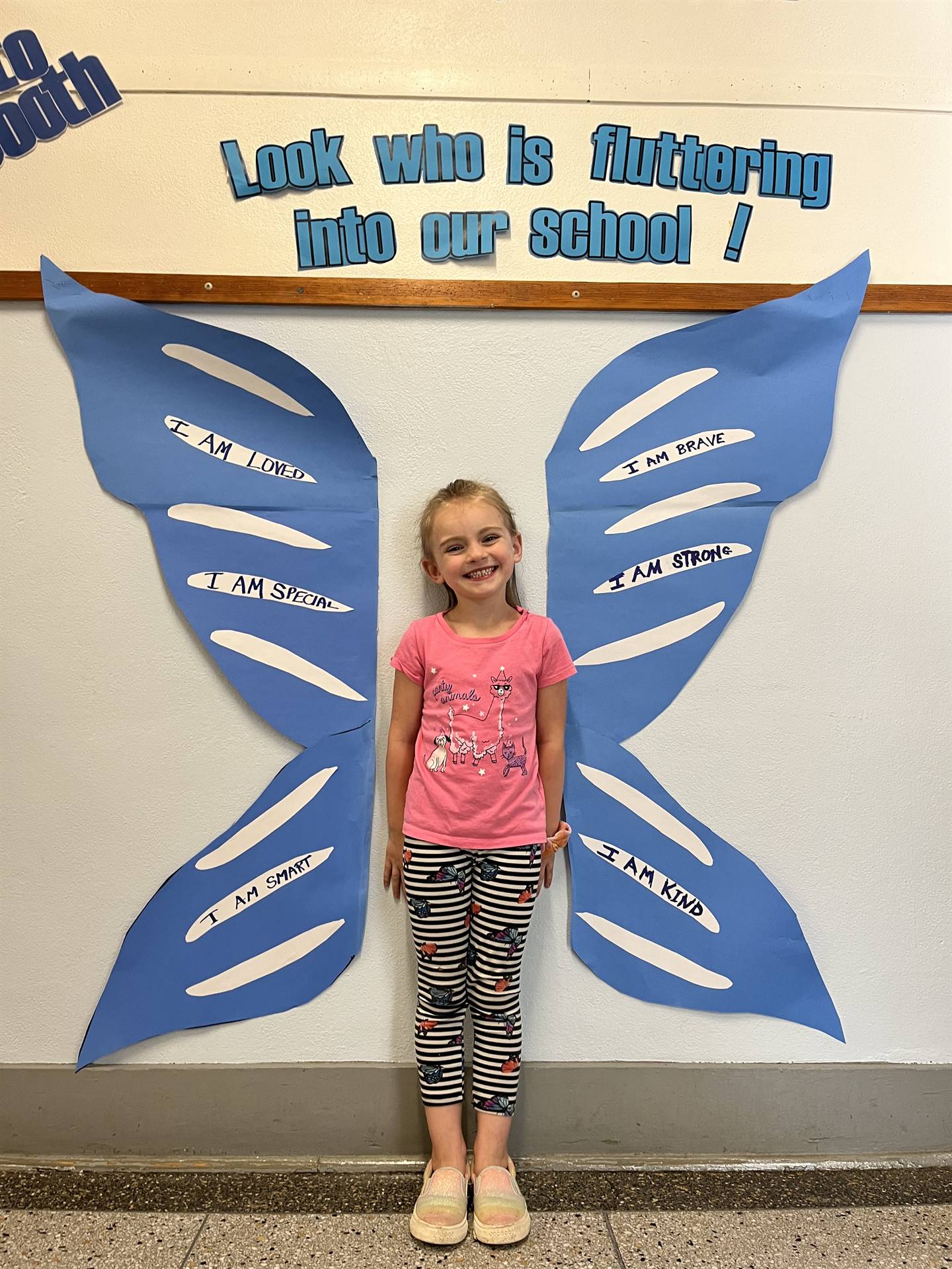 student standing between butterfly wings with sign on top saying "look who is fluttering into our sc