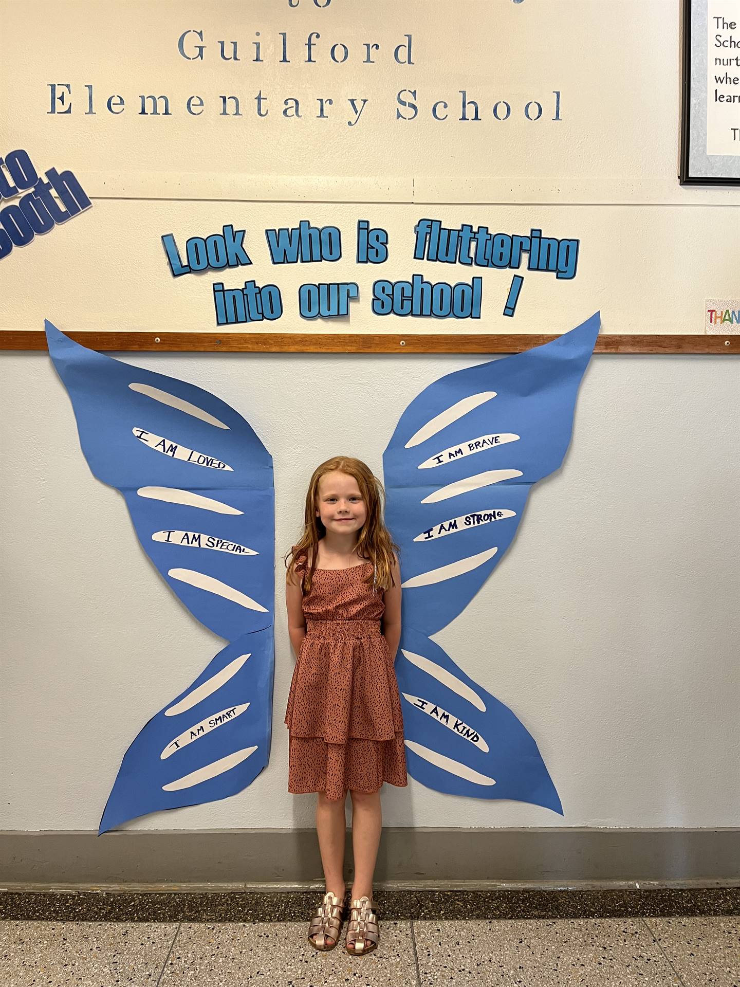 student standing between butterfly wings with sign on top saying "look who is fluttering into our sc