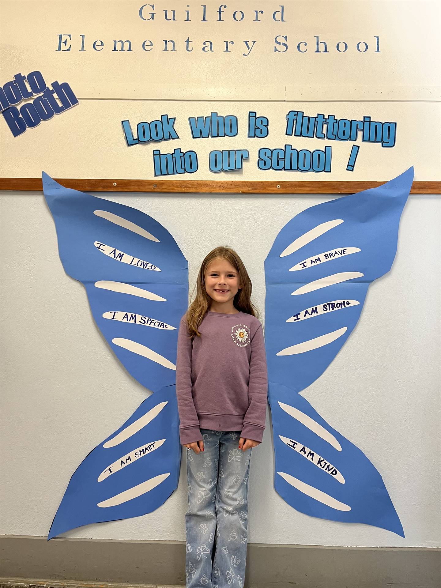 student standing between butterfly wings with sign on top saying "look who is fluttering into our sc