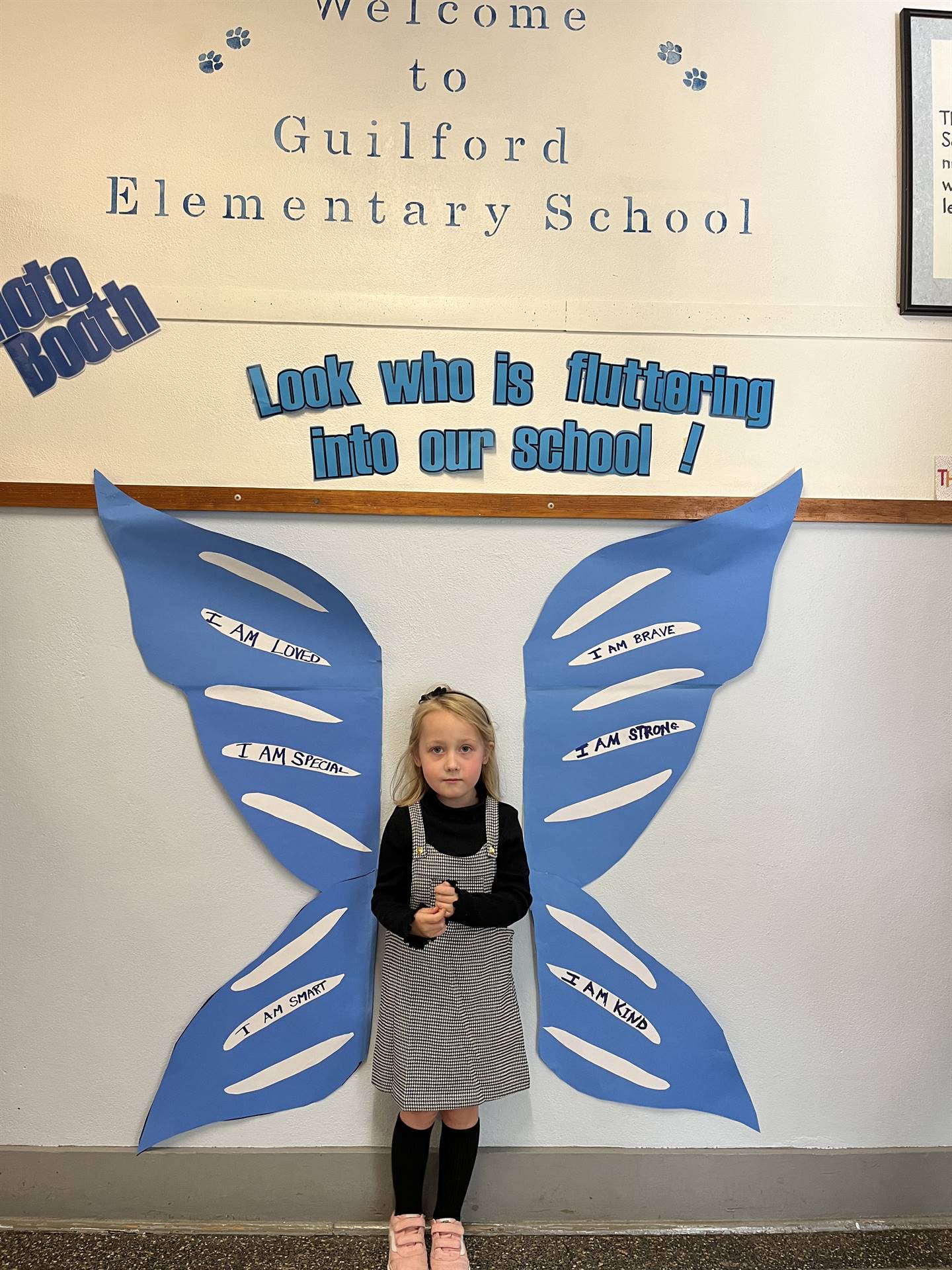 student standing between butterfly wings with sign on top saying "look who is fluttering into our sc