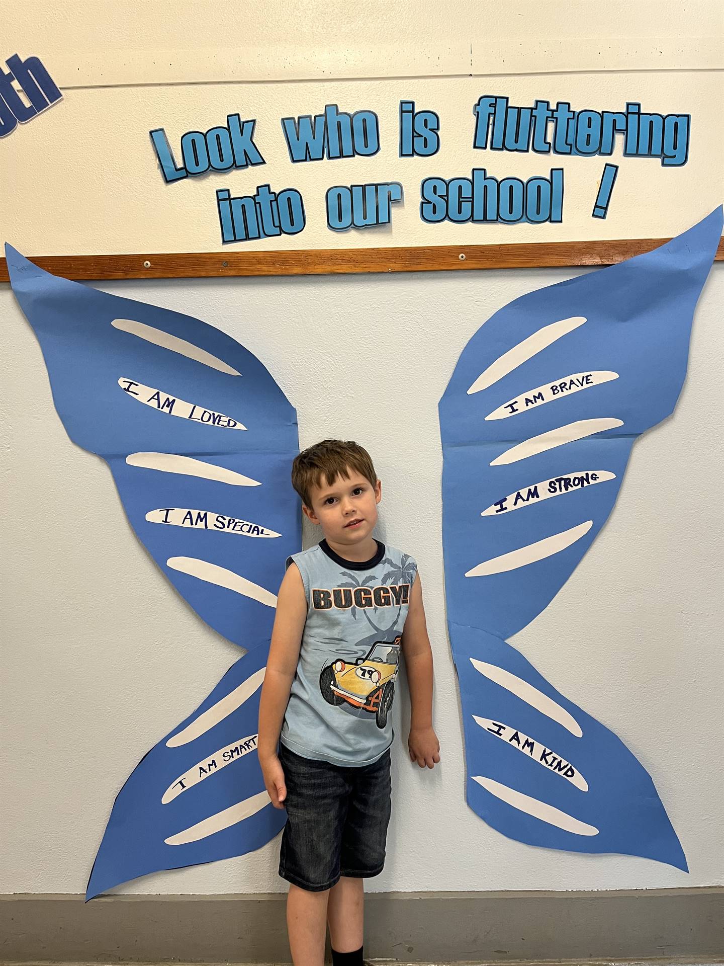 student standing between butterfly wings with sign on top saying "look who is fluttering into our sc