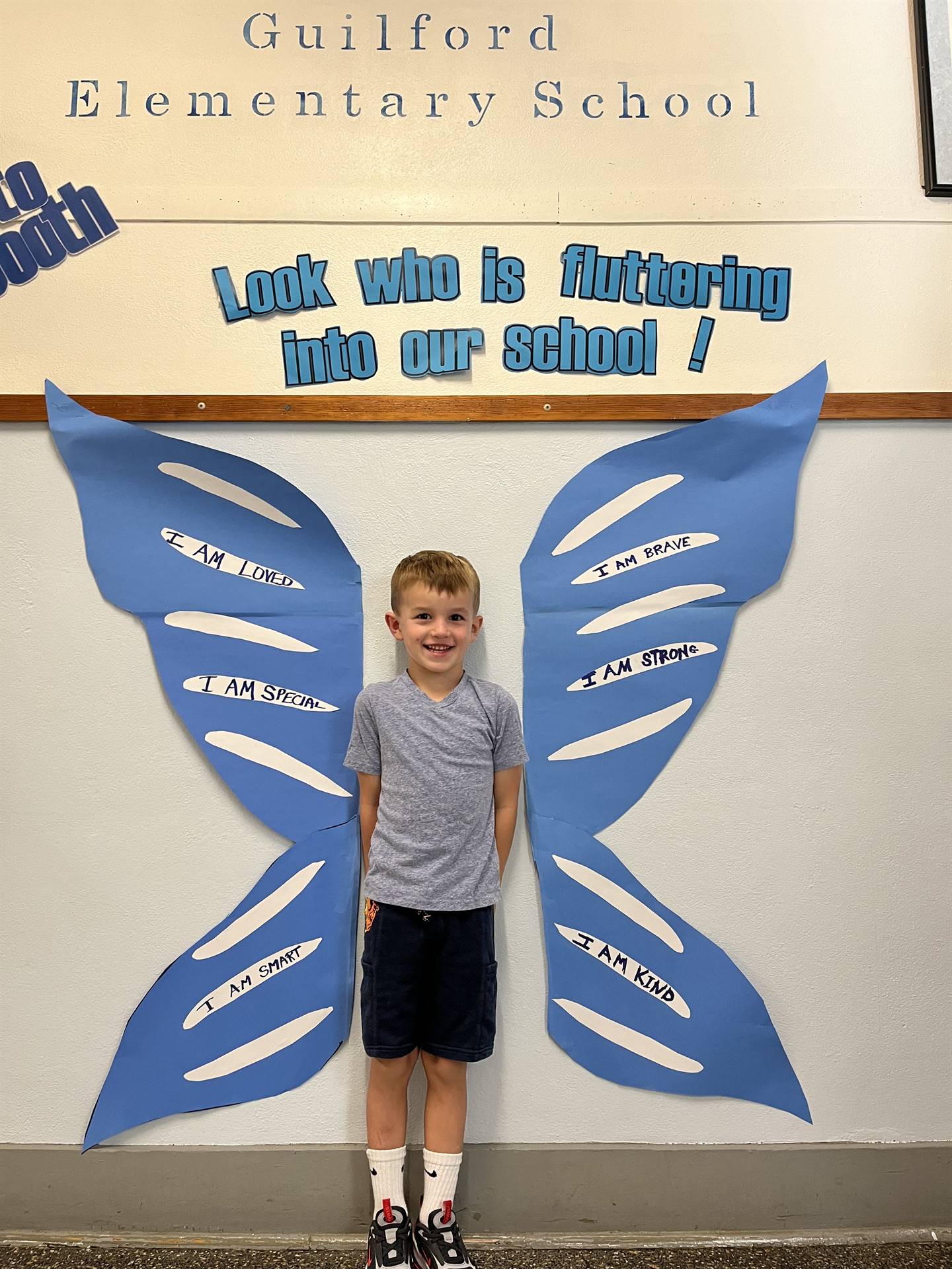 student standing between butterfly wings with sign on top saying "look who is fluttering into our sc