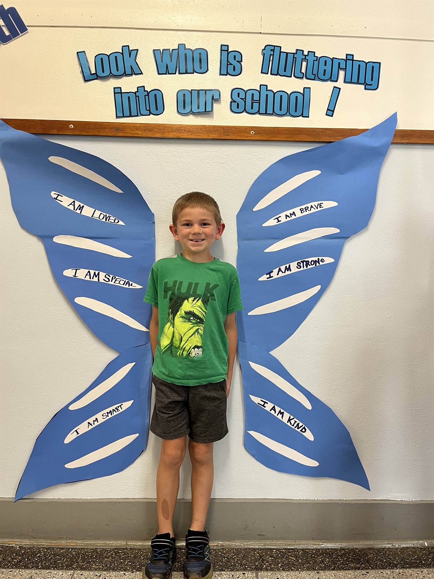 student standing between butterfly wings with sign on top saying "look who is fluttering into our sc