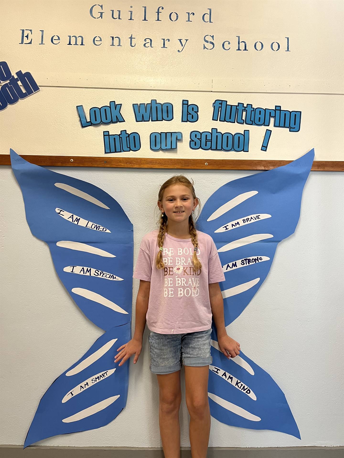 student standing between butterfly wings with sign on top saying "look who is fluttering into our sc