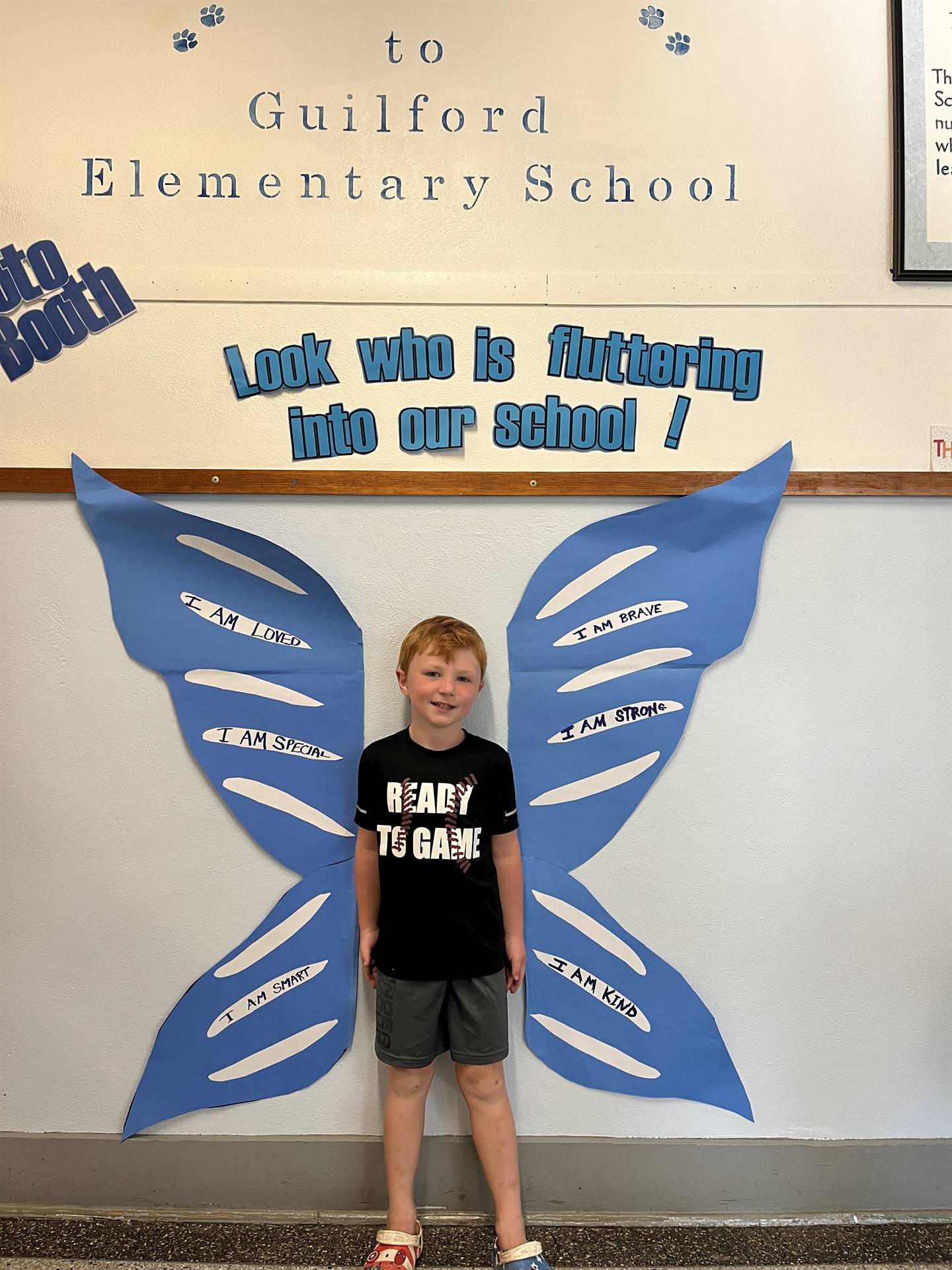 student standing between butterfly wings with sign on top saying "look who is fluttering into our sc