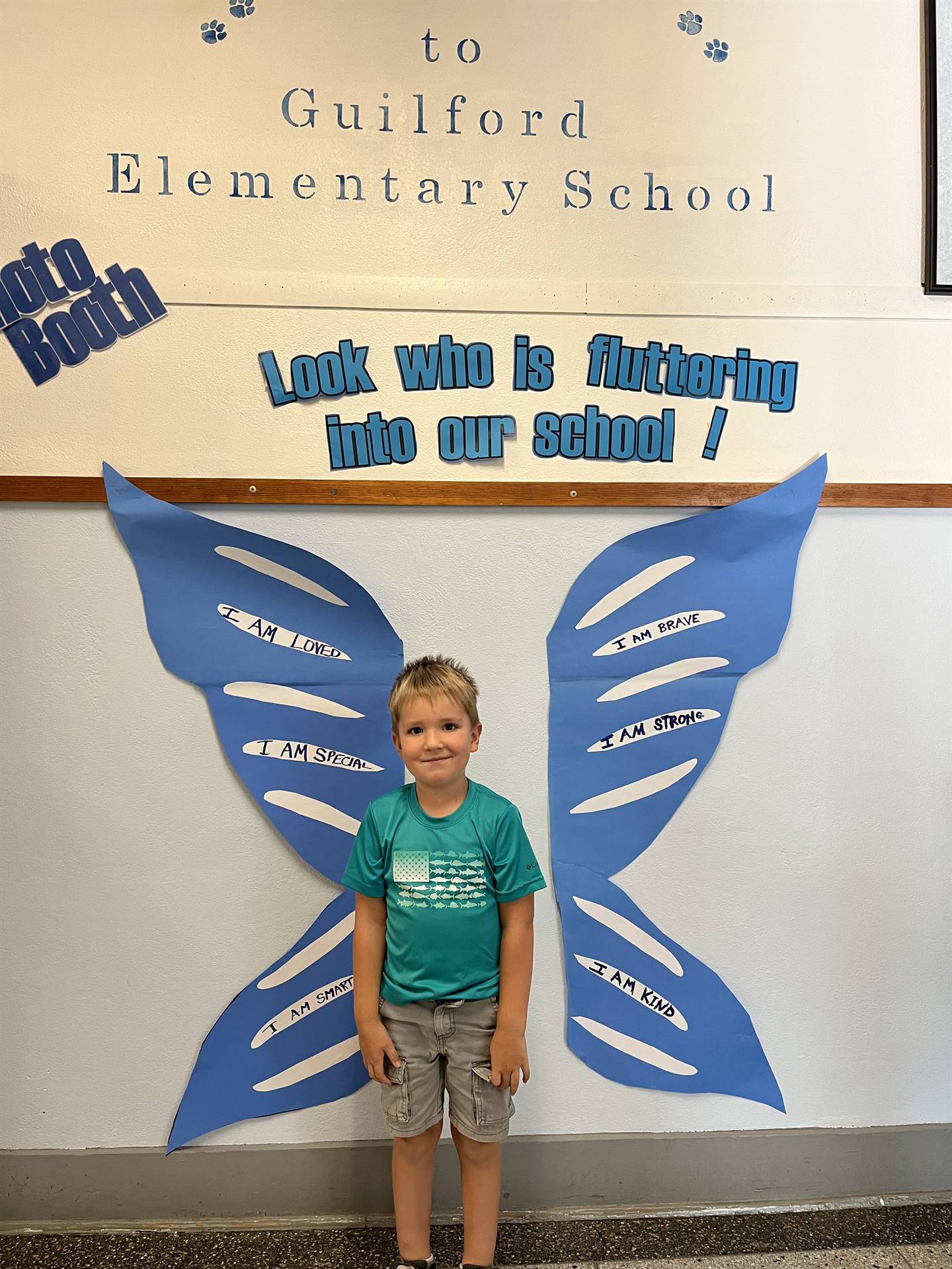 student standing between butterfly wings with sign on top saying "look who is fluttering into our sc