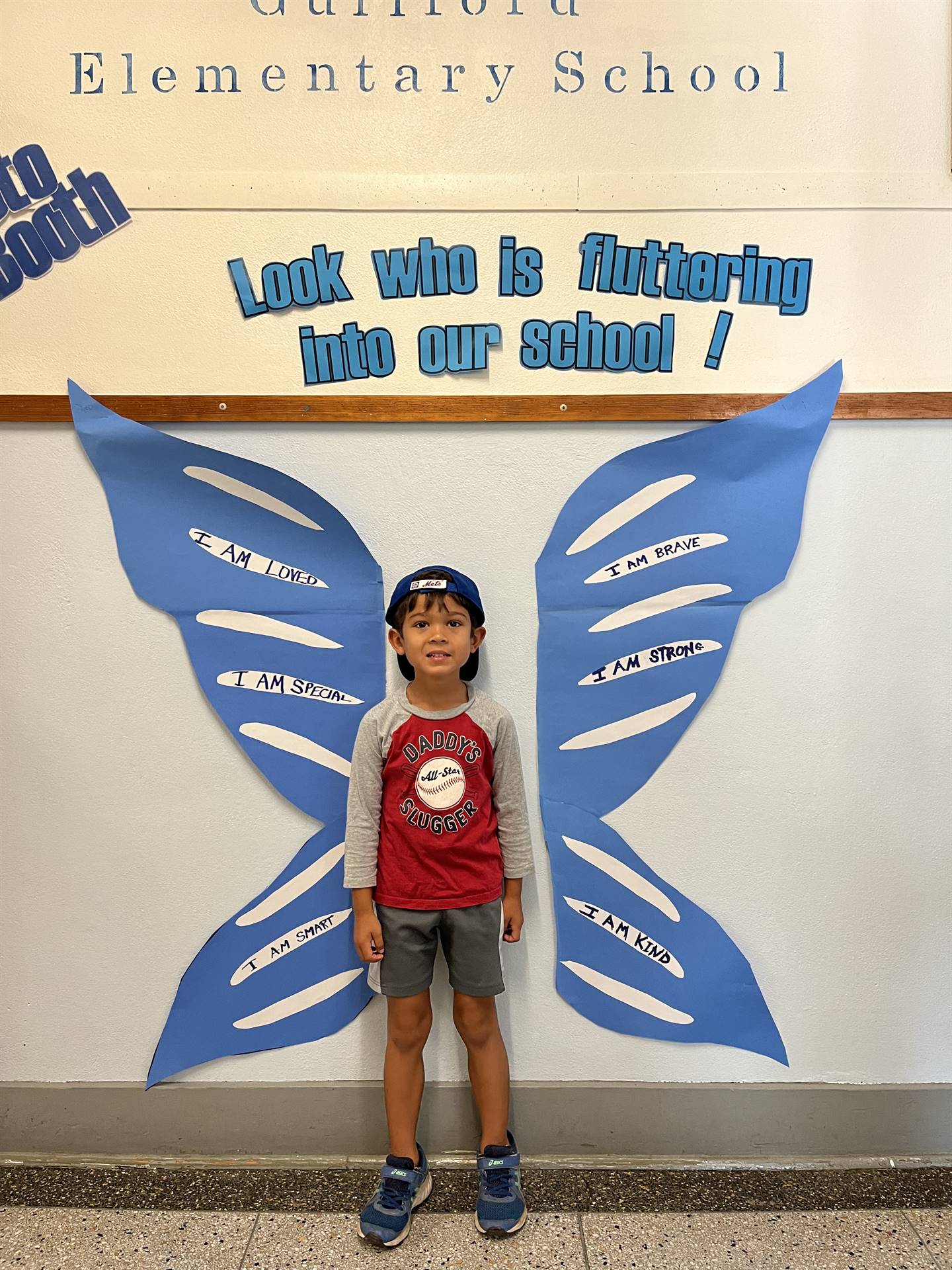 student standing between butterfly wings with sign on top saying "look who is fluttering into our sc