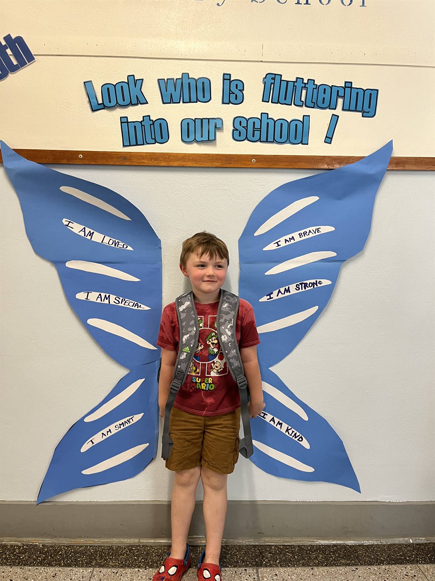 student standing between butterfly wings with sign on top saying "look who is fluttering into our sc