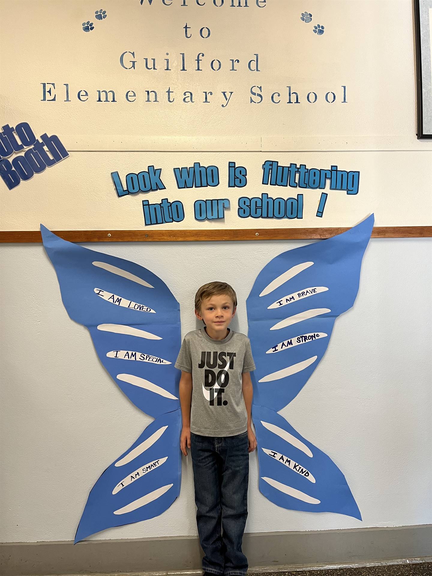 student standing between butterfly wings with sign on top saying "look who is fluttering into our sc