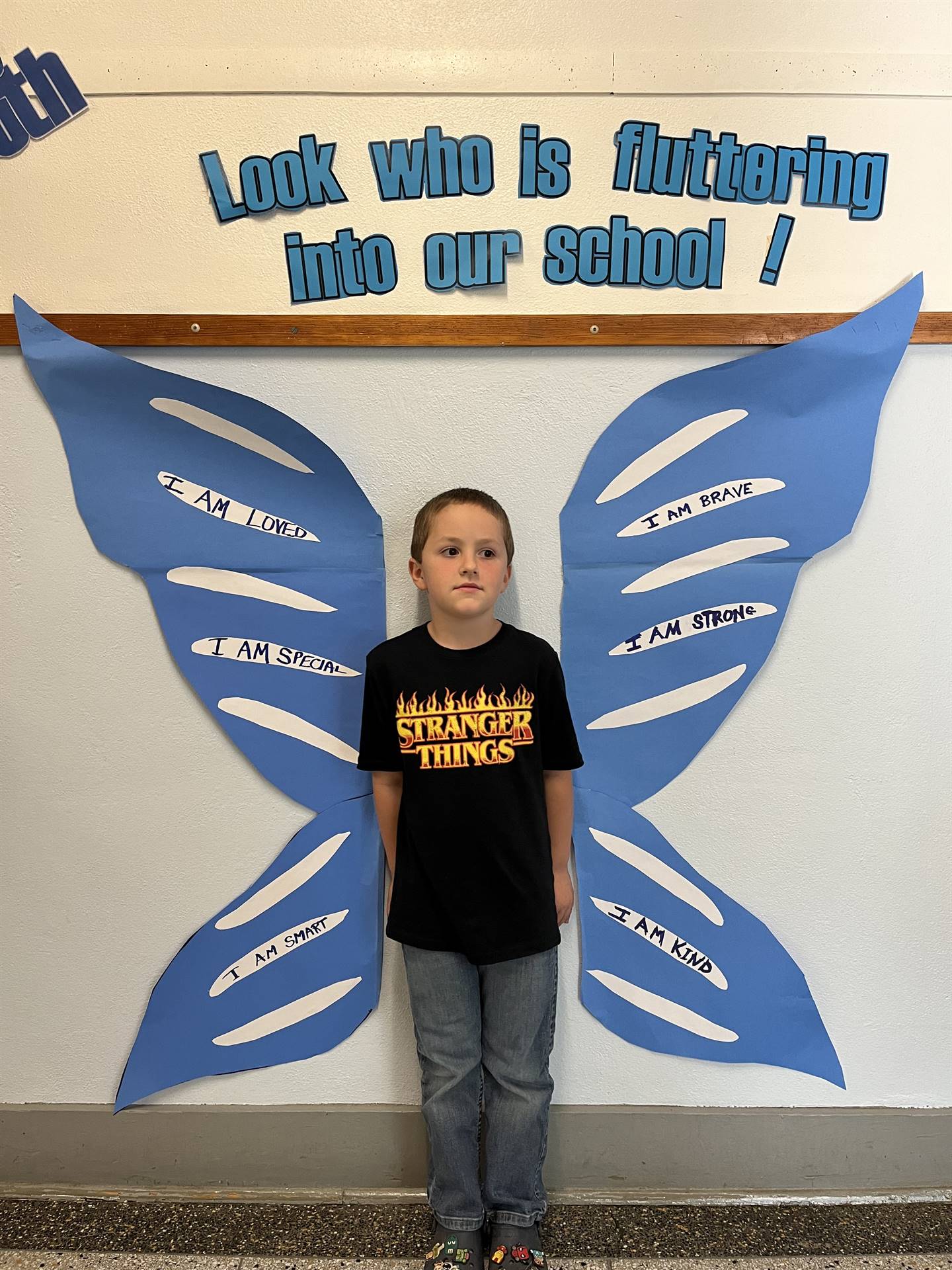 student standing between butterfly wings with sign on top saying "look who is fluttering into our sc